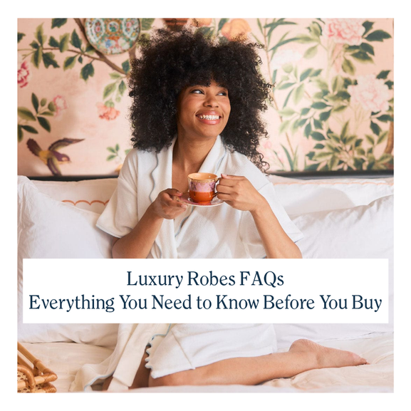 A smiling woman in a crisp white robe sitting on a bed and holding a teacup.