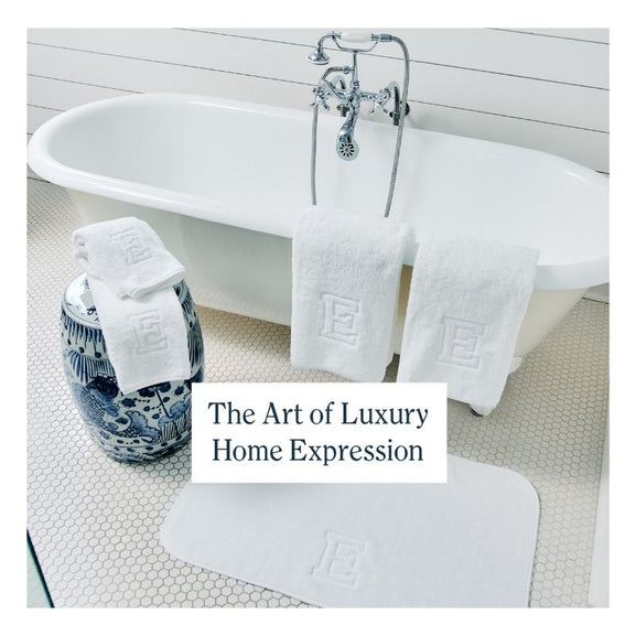 White monogrammed bath towels and bath mat displayed beside a freestanding tub with text reading “The Art of Luxury Home Expression”