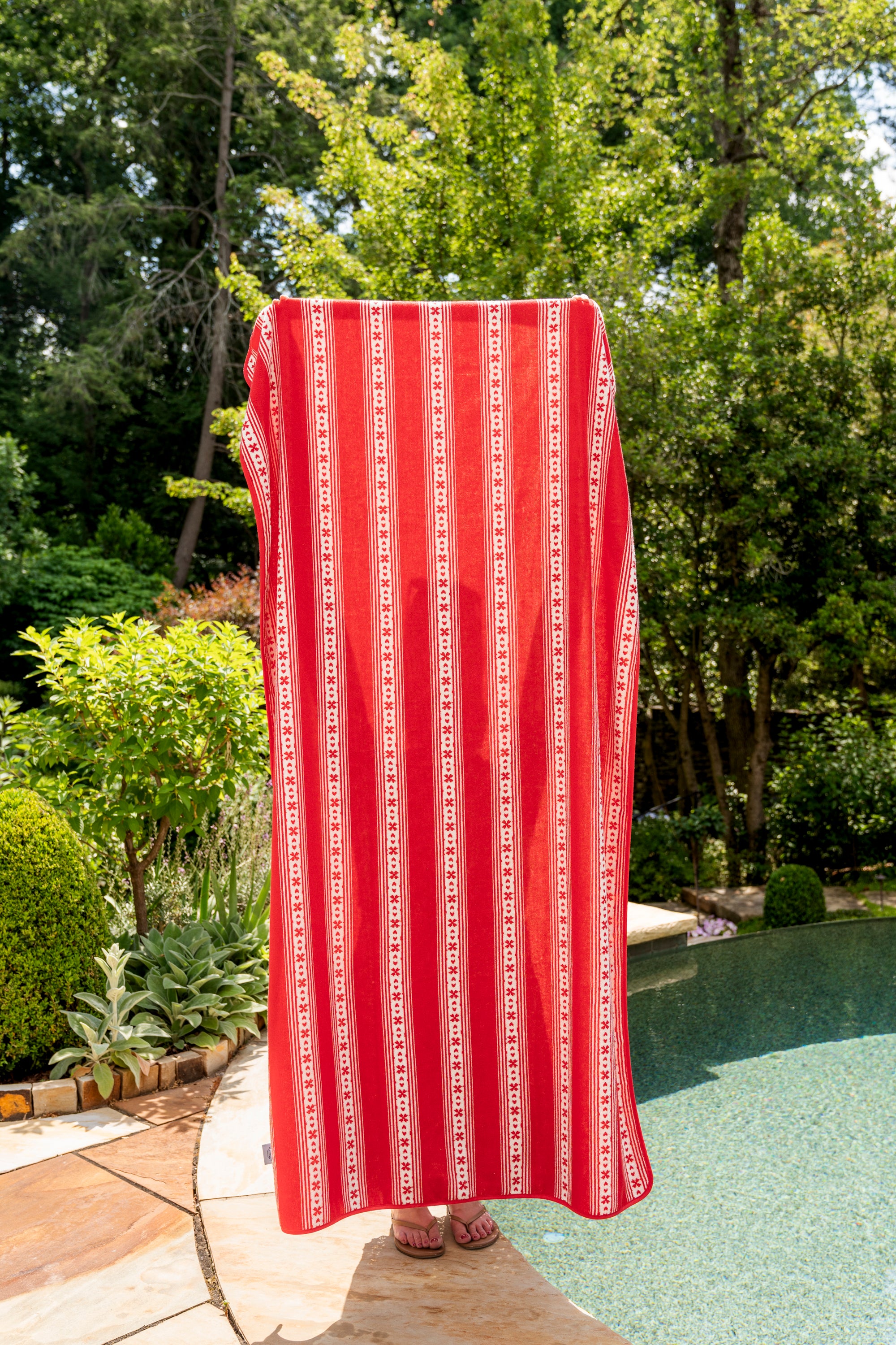 Red and white patterned towel draped over a chair by a poolside with greenery in the background