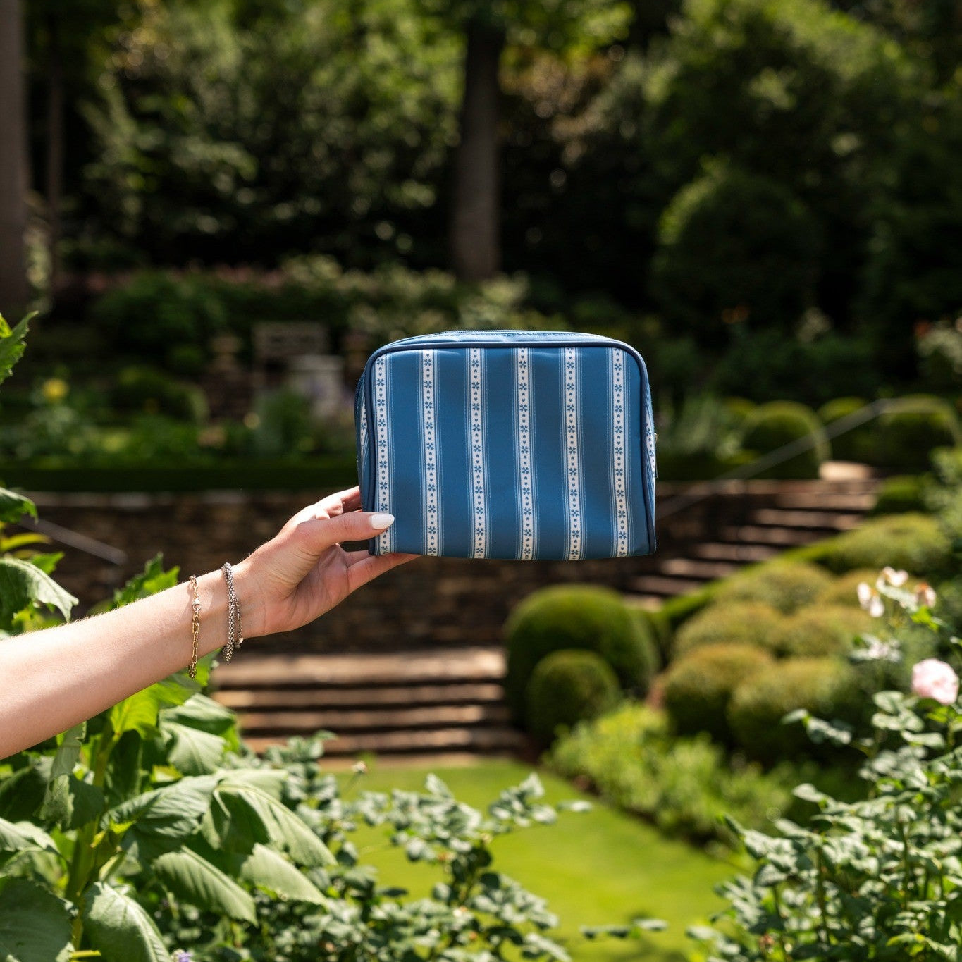 Hand holding a blue pouch with white patterns in a garden setting