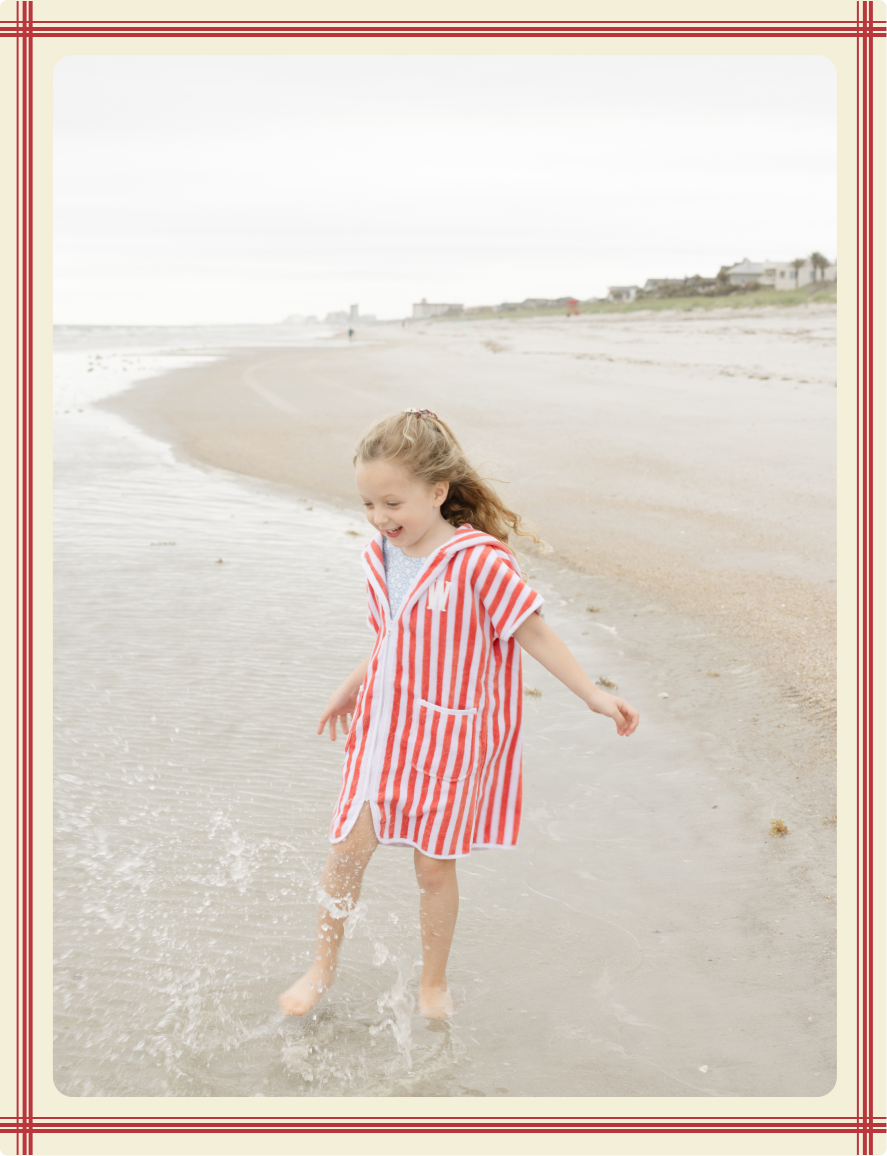 Young girl in a red and white striped dress playing on a beach.