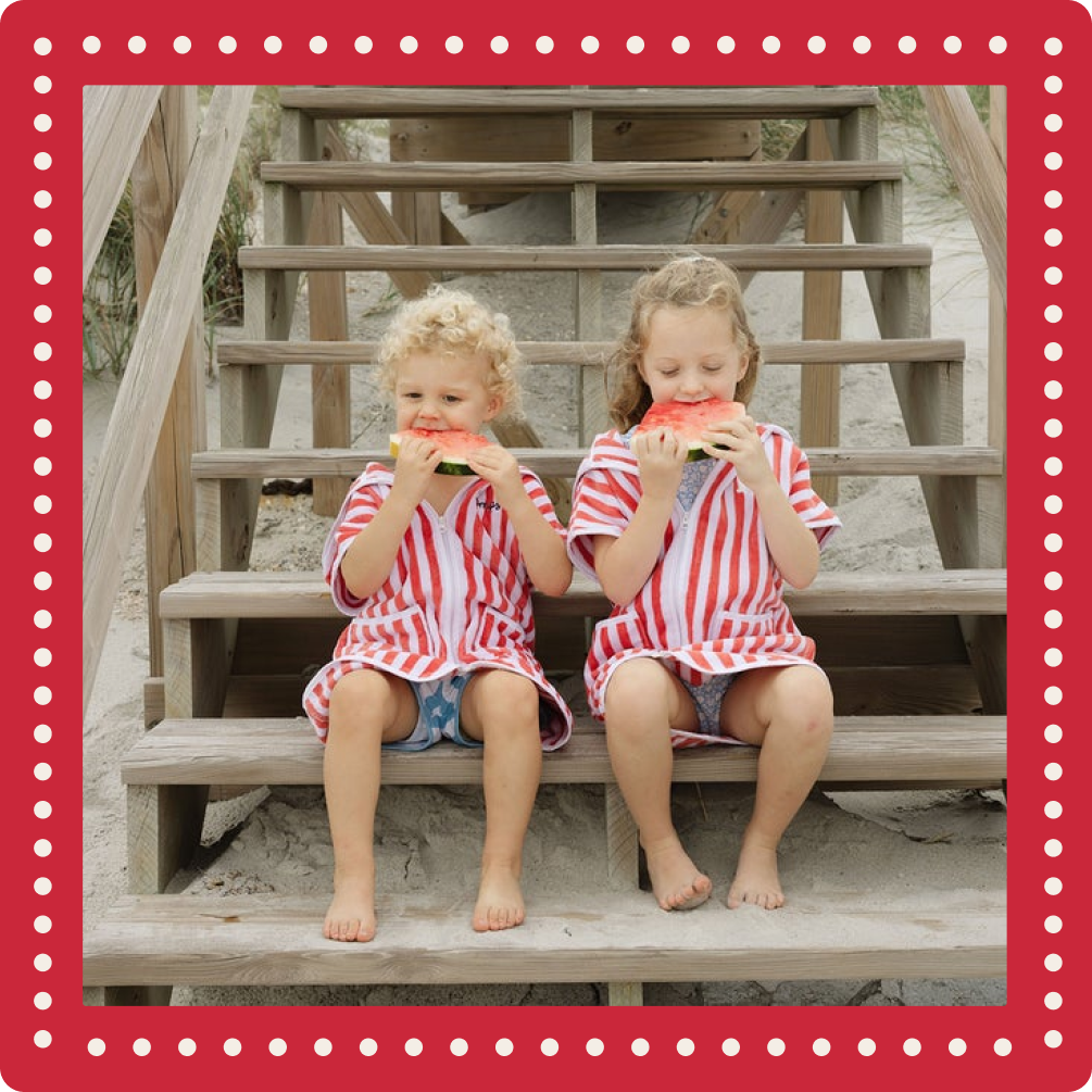 Two children in matching striped outfits sitting on wooden steps at the beach.