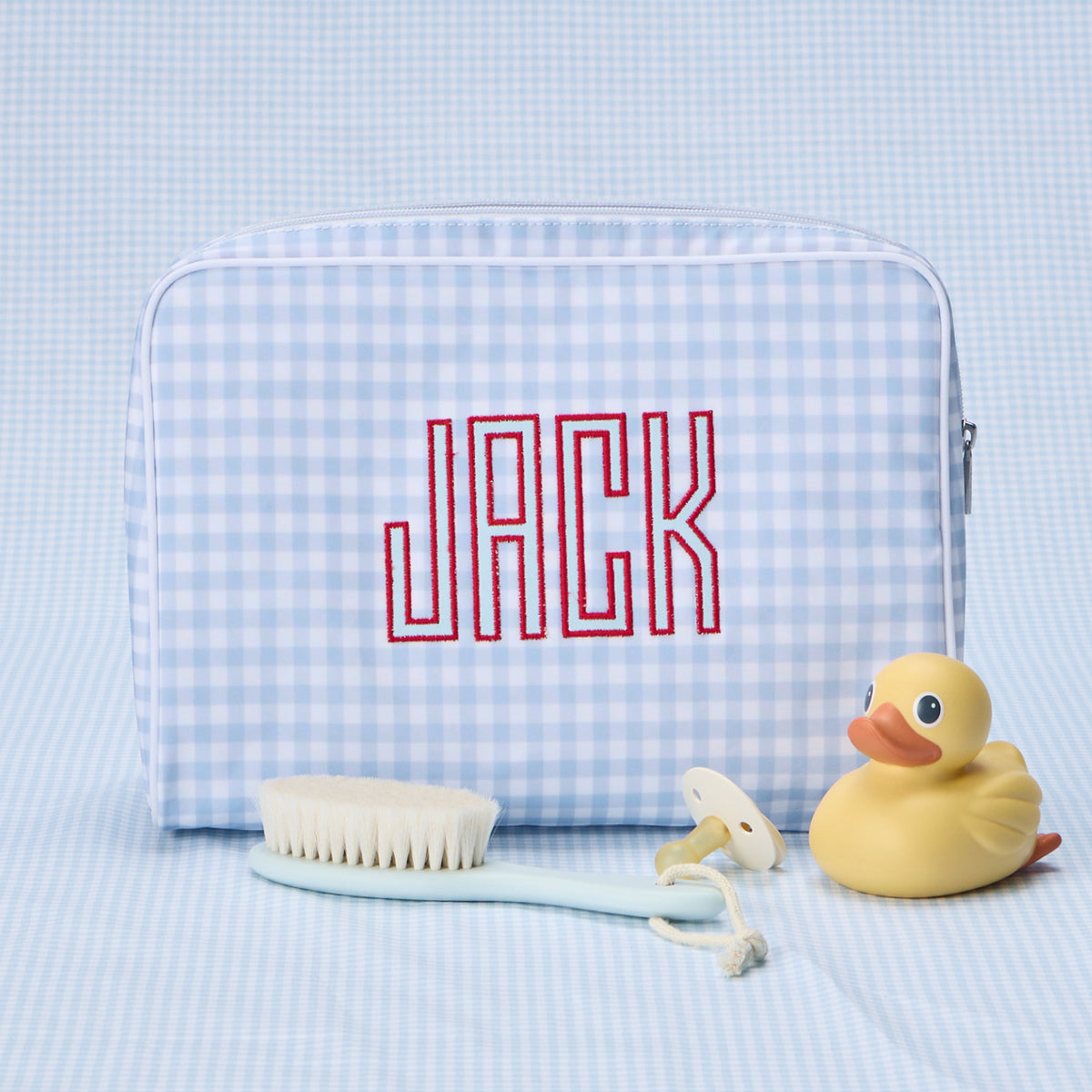 A light blue gingham toiletry bag with the name "JACK" embroidered in red stitching, displayed next to a rubber duck.