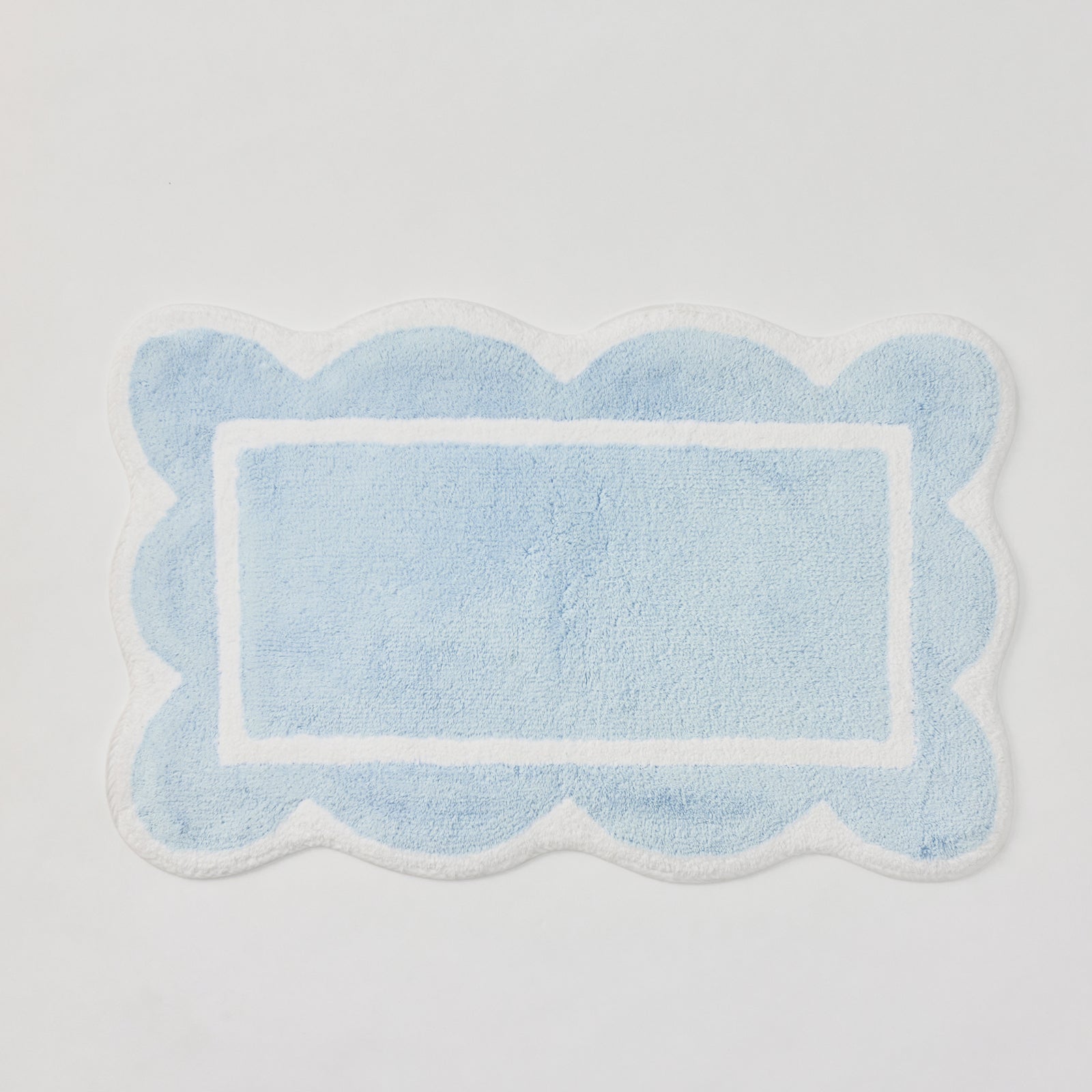 A light blue plush bath rug with scalloped edges