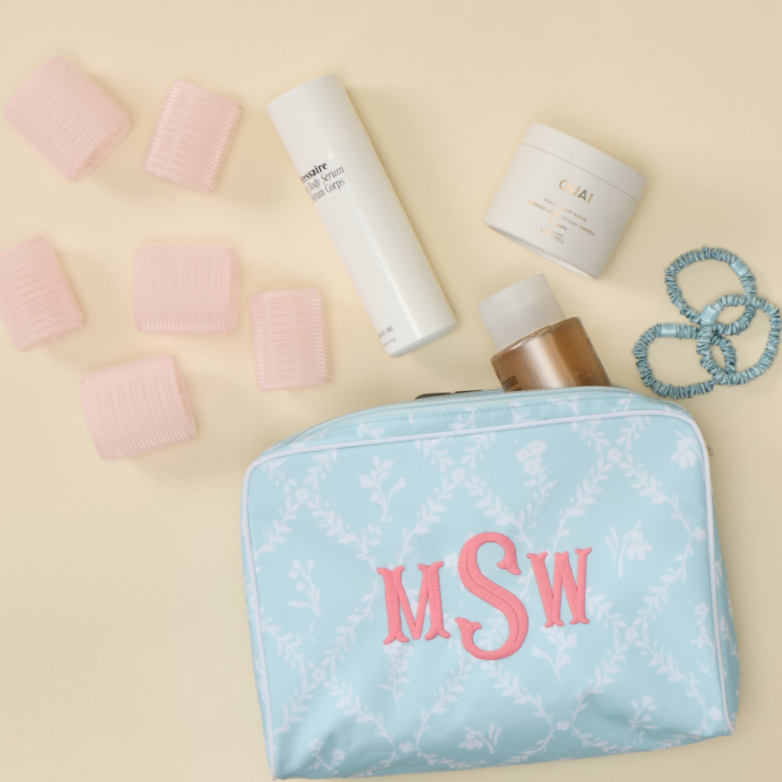 A light blue, floral trellis patterned toiletry bag with a pink "MSW" monogram, surrounded by hair products and accessories.