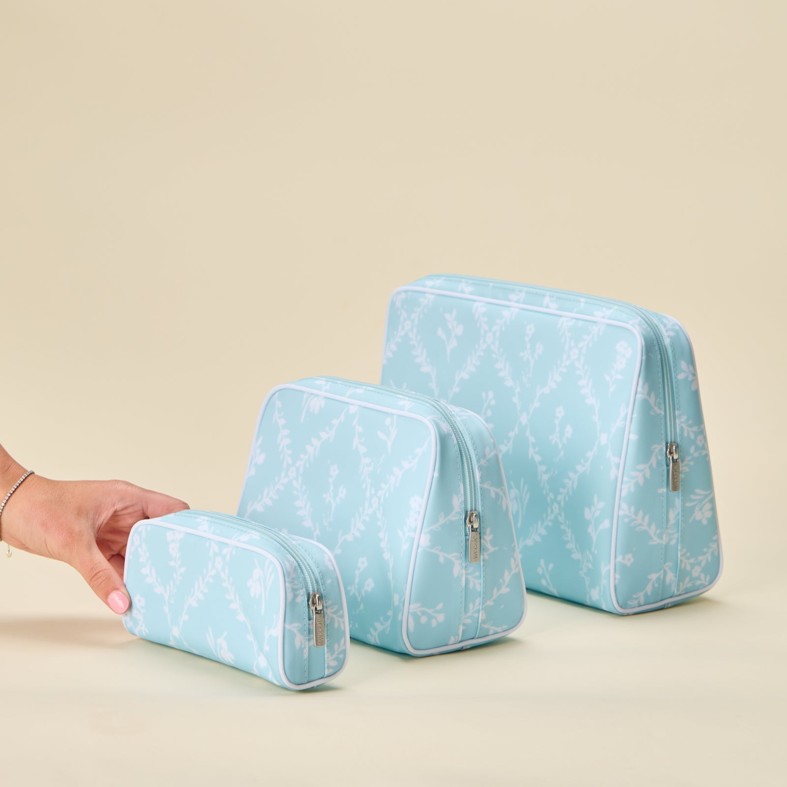 A hand places the small Blue Trellis patterned toiletry bag next to the medium and large sizes in the same design.
