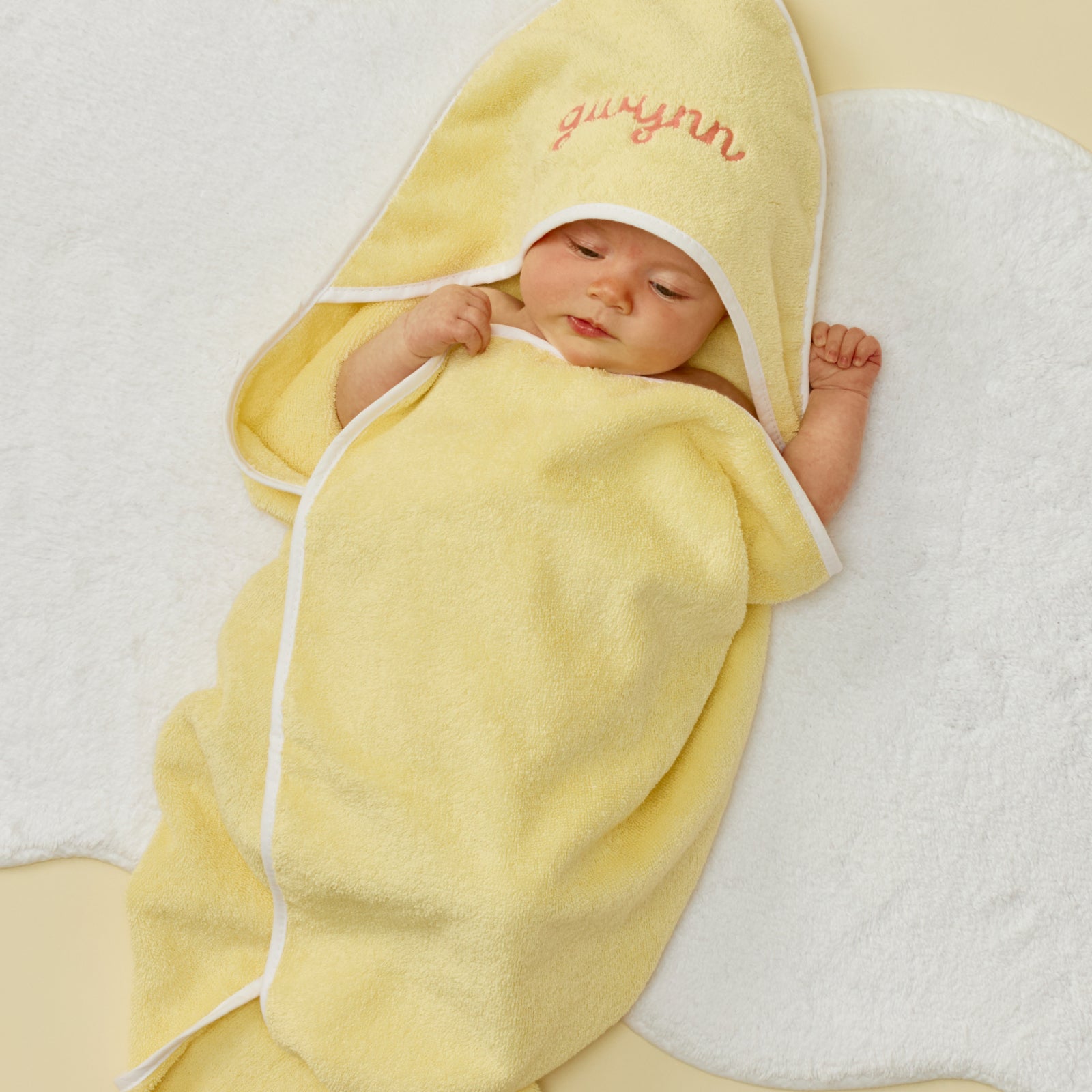 Baby wrapped in a yellow hooded towel with white trim and pink gwynn embroidery.