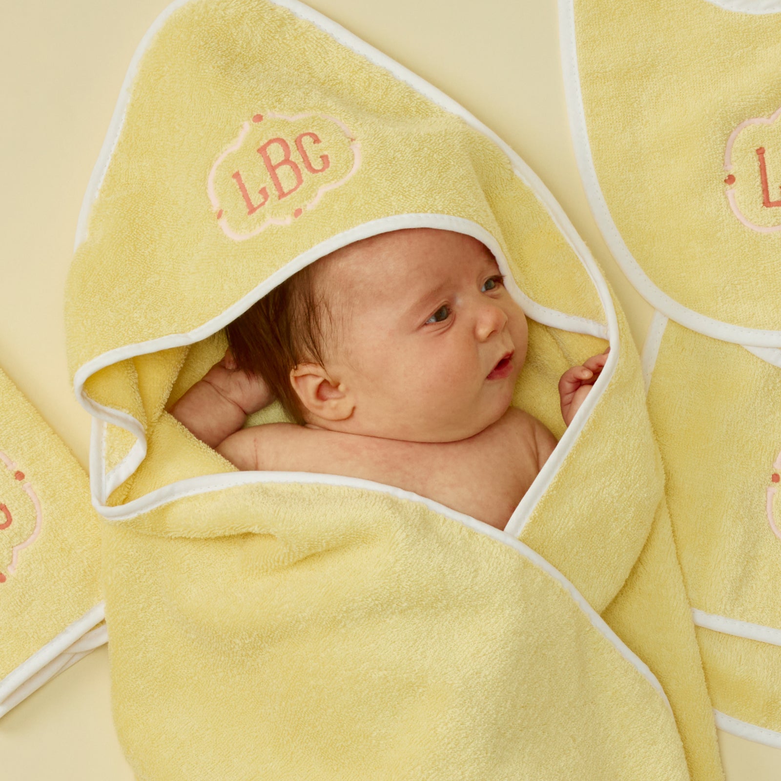 Baby wrapped in a buttercup yellow hooded towel with white piping and pink LBC monogram.