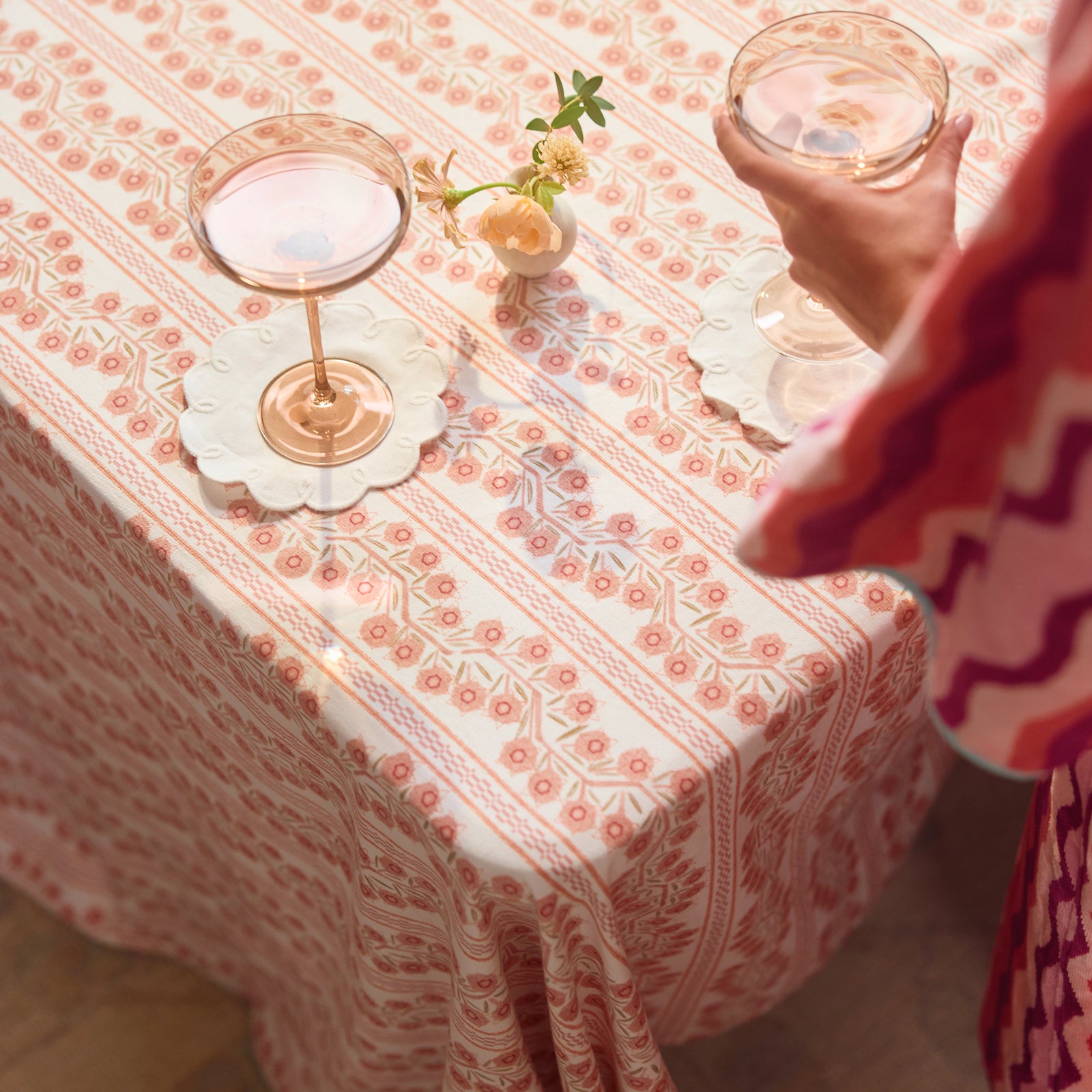A view of the Climbing Vine tablecloth, with the cocktail napkin and wine glass on top of it. A woman in squiggly robe stands next to the table.