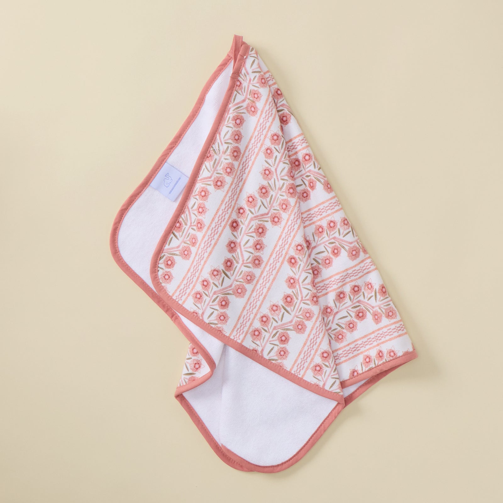 A hanging kitchen towel featuring a pink and peach floral climbing vine pattern and solid pink trim.