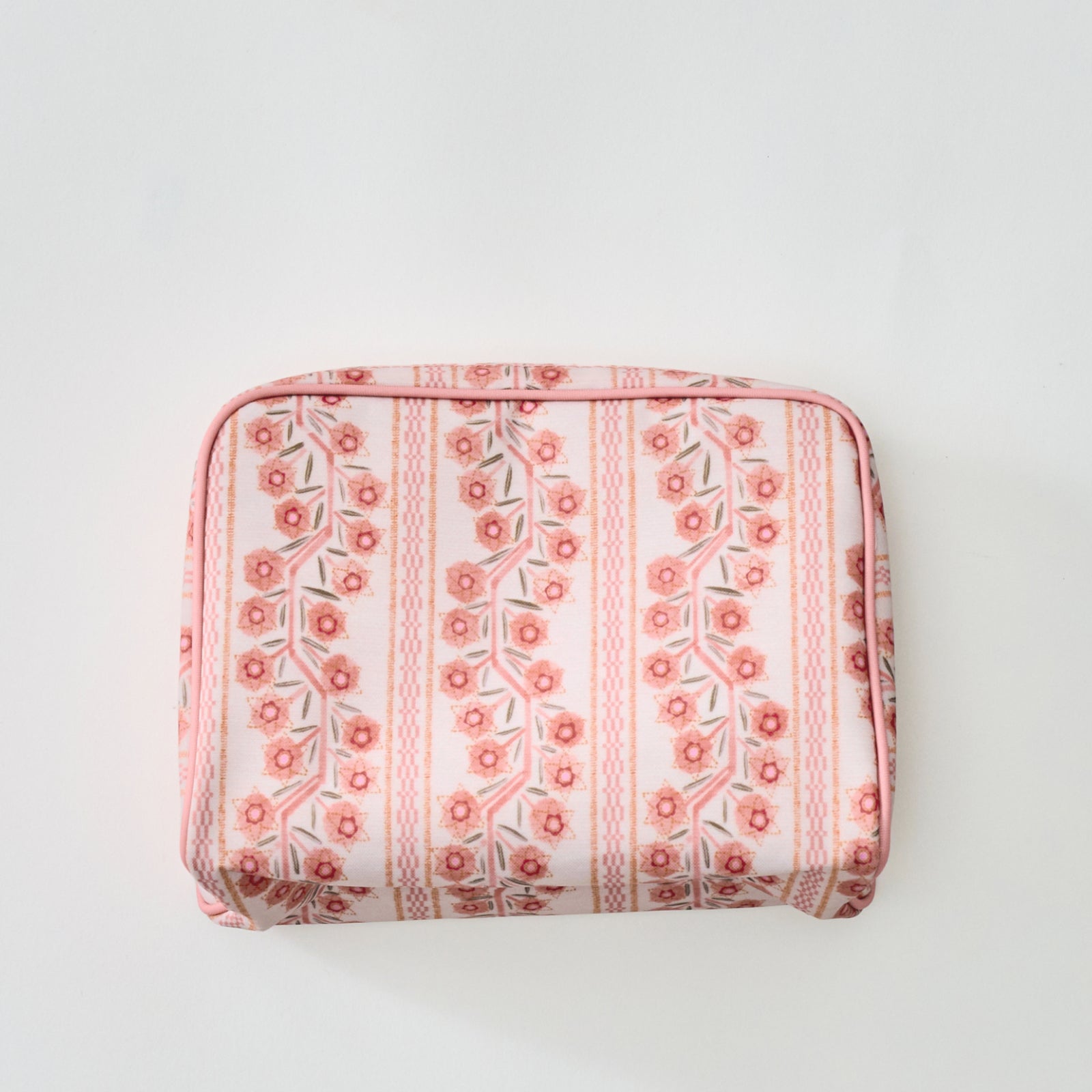 A rectangular toiletry bag featuring a pink and coral floral stripe pattern with light pink piping, photographed from directly above against a plain light background