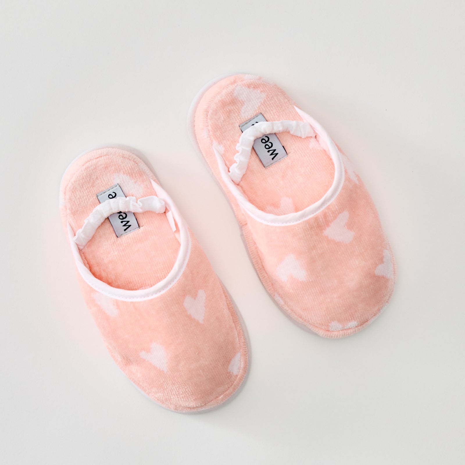 Fluffy coral pink slippers with white hearts and a ruffled elastic strap.
