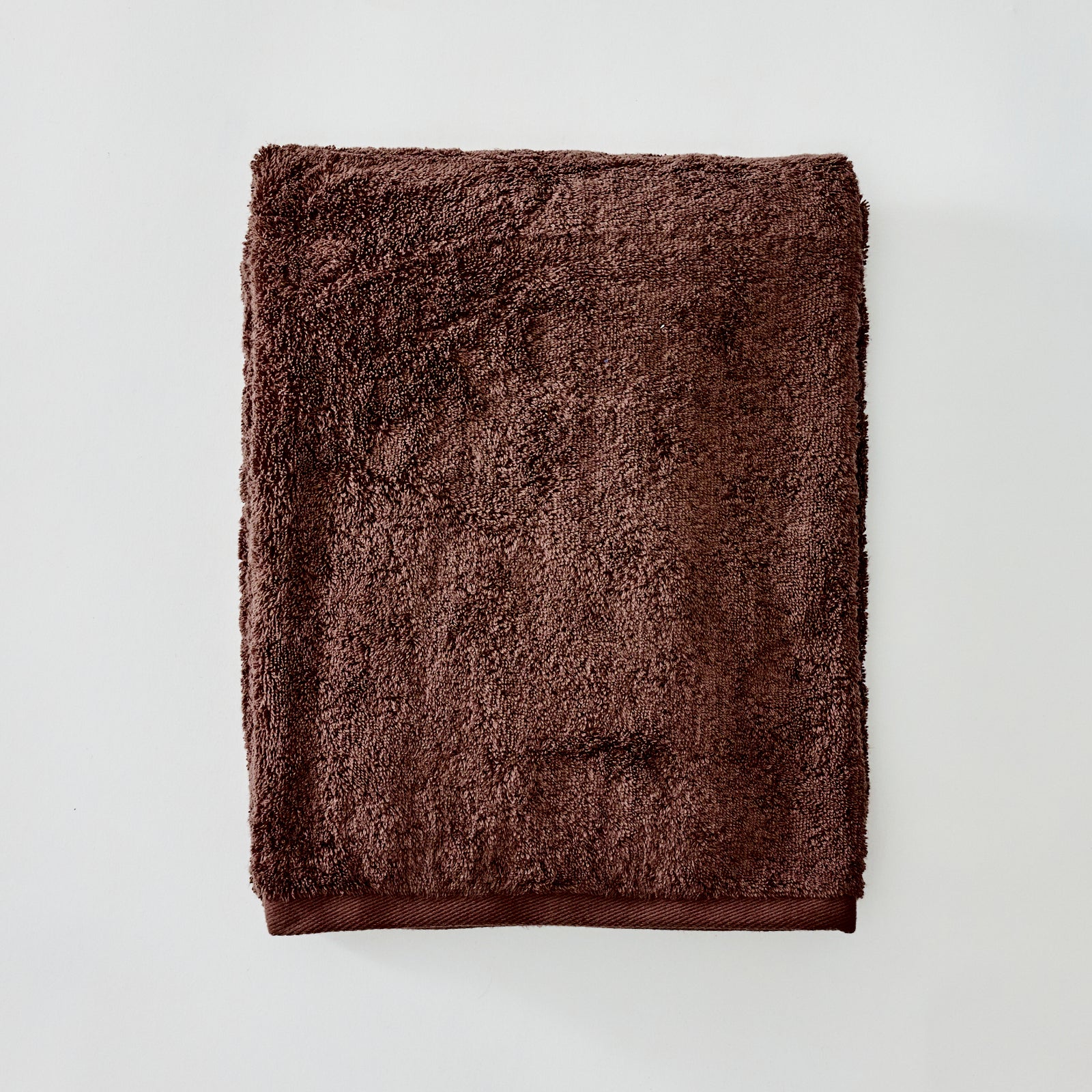 A folded brown terry cloth towel with a ribbed solid brown border, displayed flat against a light gray background.