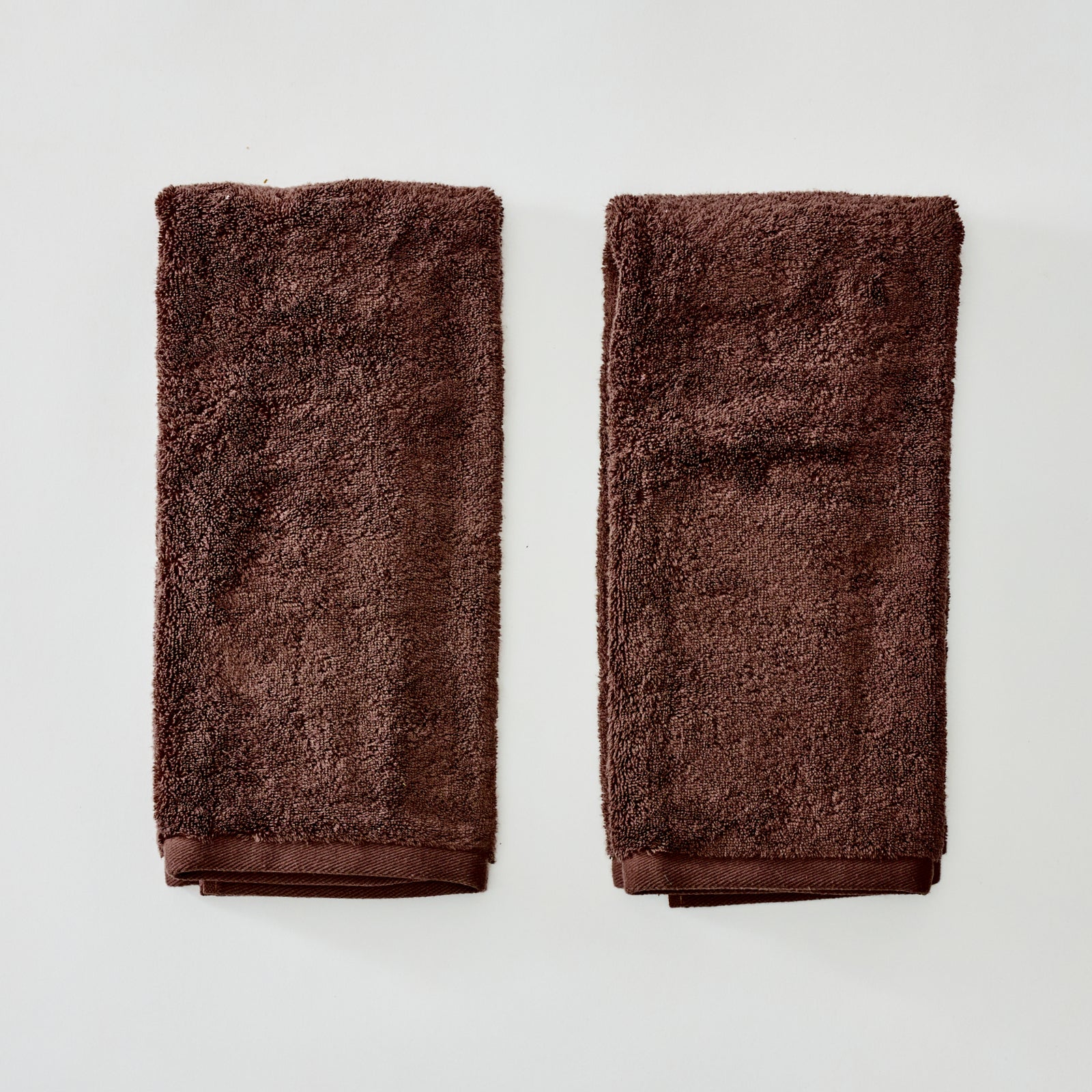 Two folded brown terry cloth towels laid side by side on a plain light background.