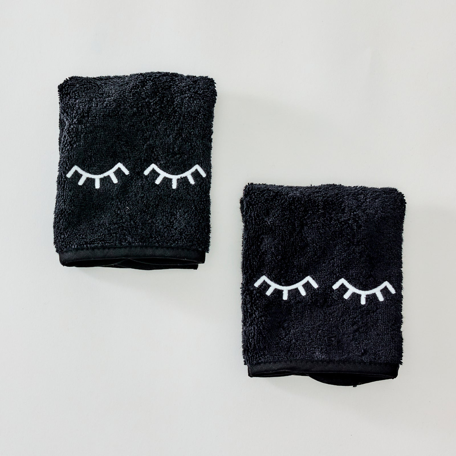 Two black towels with white embroidered closed-eye designs, displayed on a clean white background.