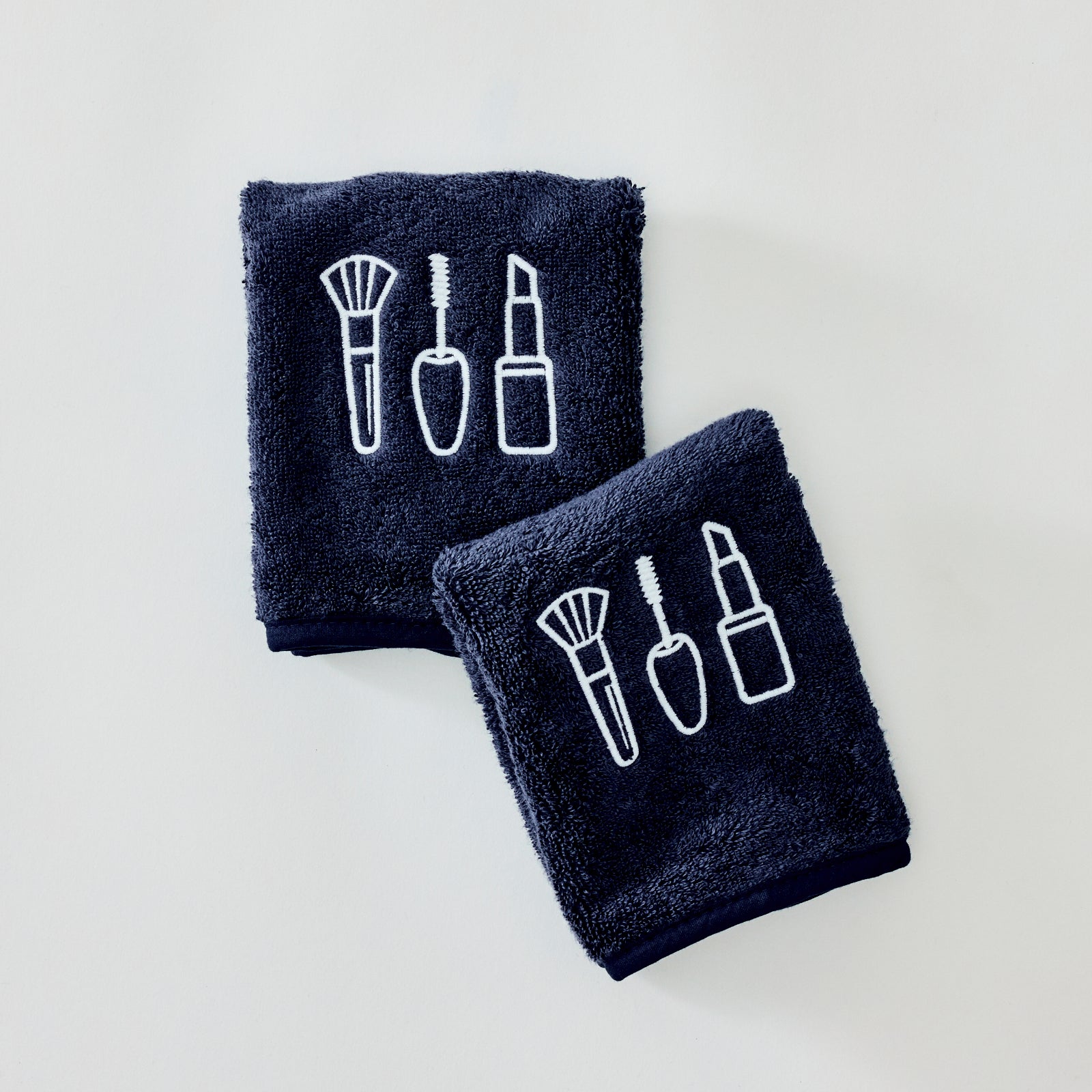 Two navy blue towels with white embroidered cosmetic icons, displayed on a clean white background.