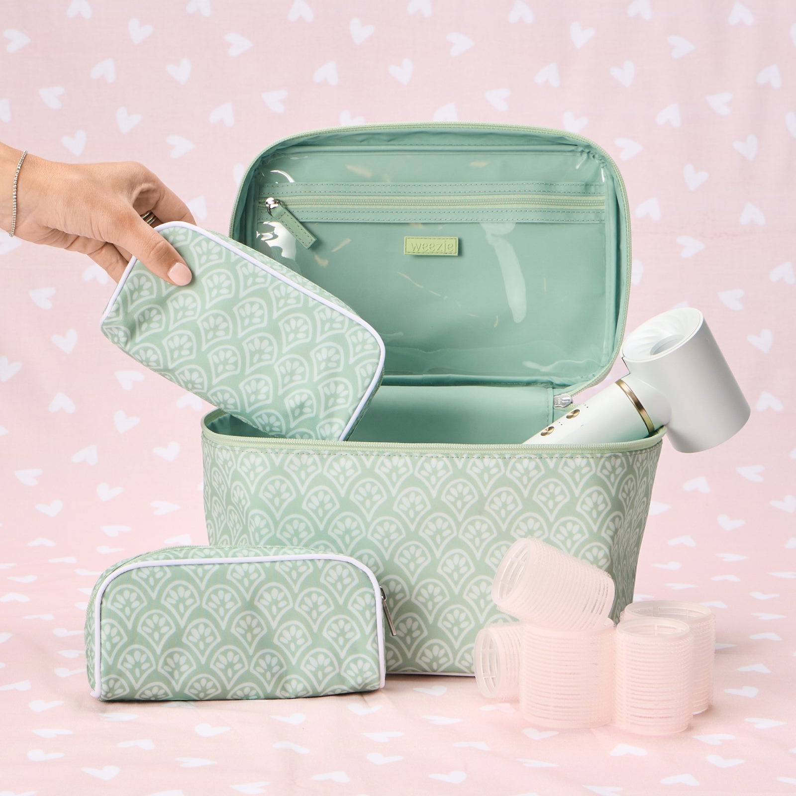 A Weezie Travel Bundle in a Green Block Print floral pattern, featuring one large vanity case and two smaller matching toiletry bags, displayed with skincare products on a neutral surface.