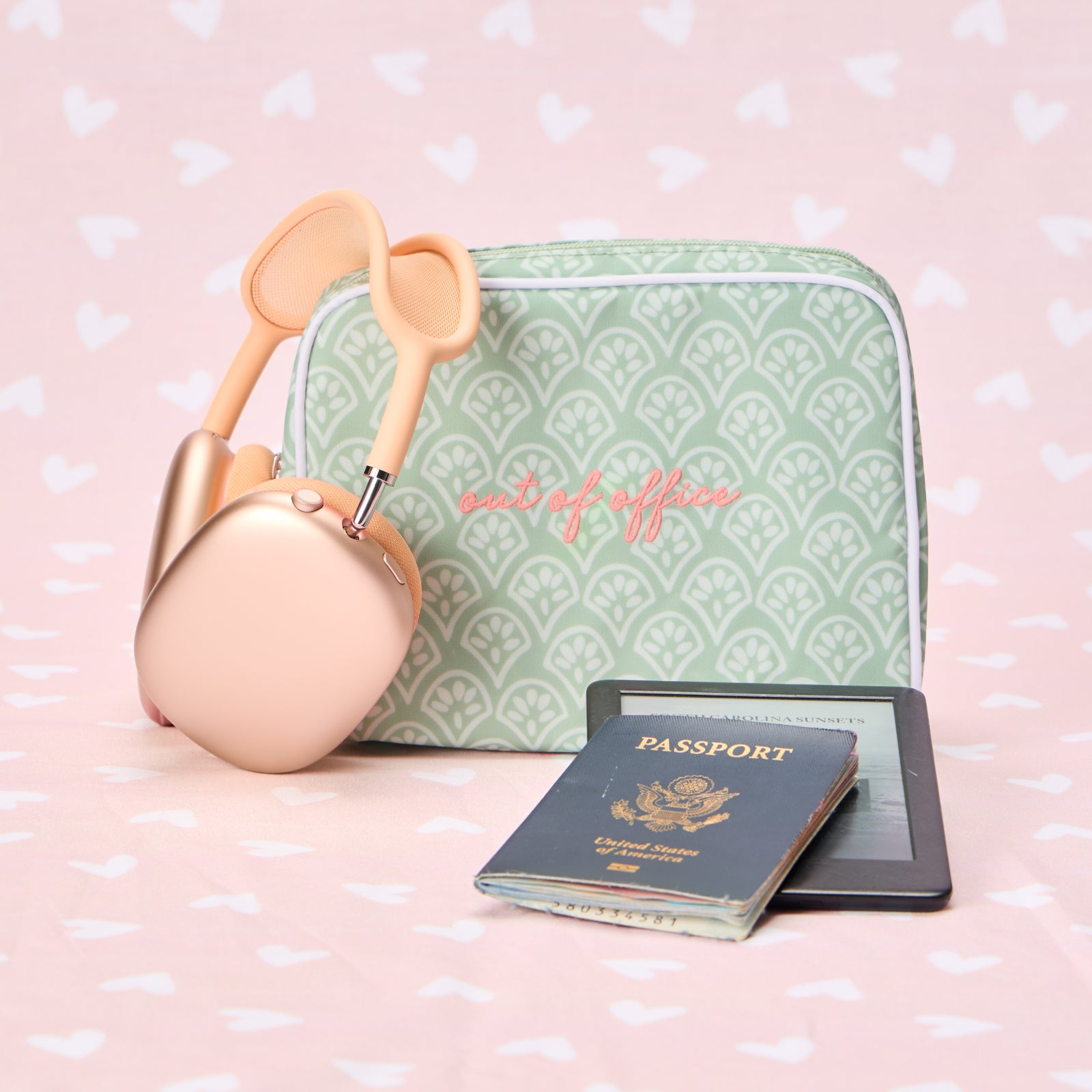A personalized Green Block Print toiletry bag labeled "out of office" next to headphones, a passport, and an e-reader.