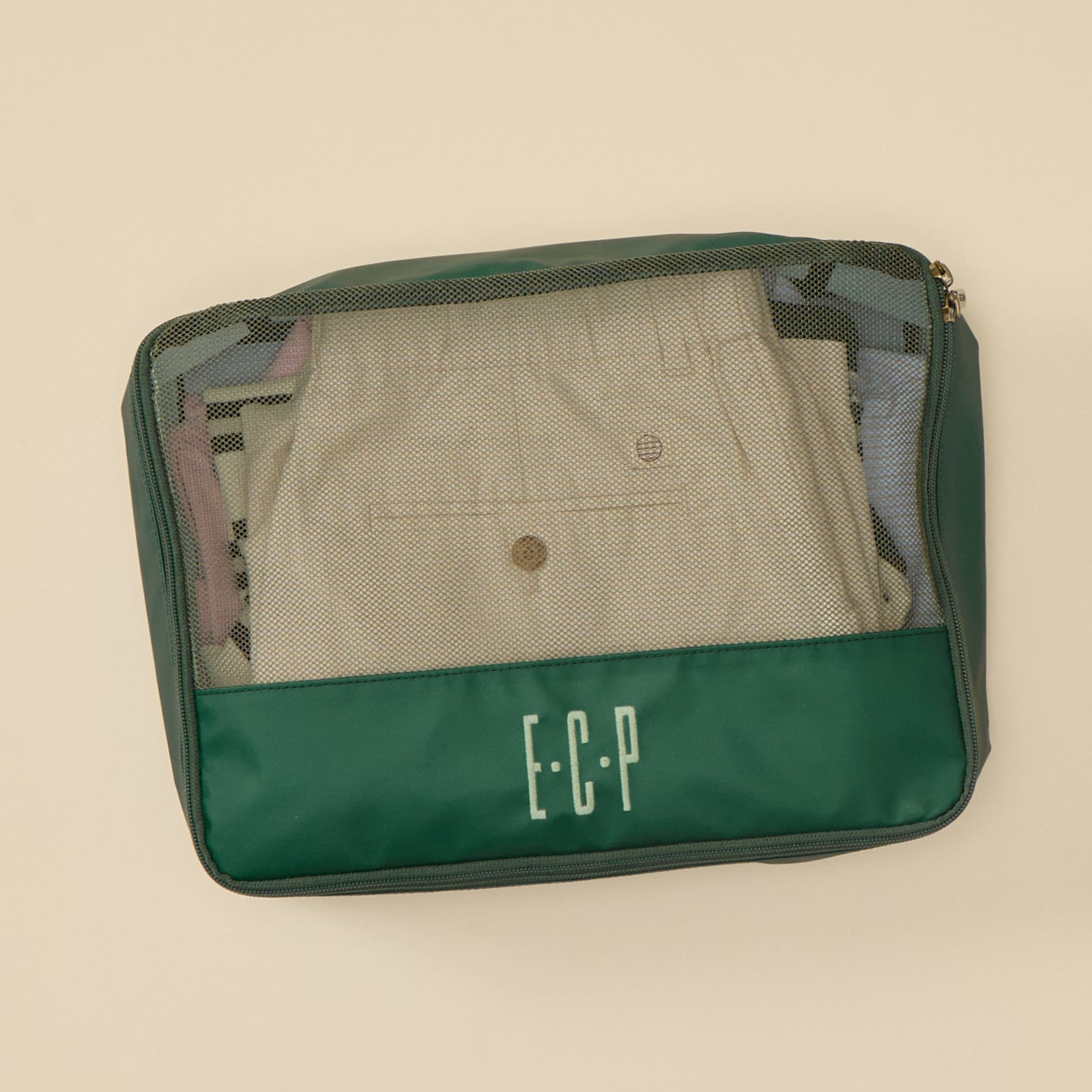 Personalized Hunter Green packing cube with 'ECP' monogram, filled with neatly folded light-colored garments.