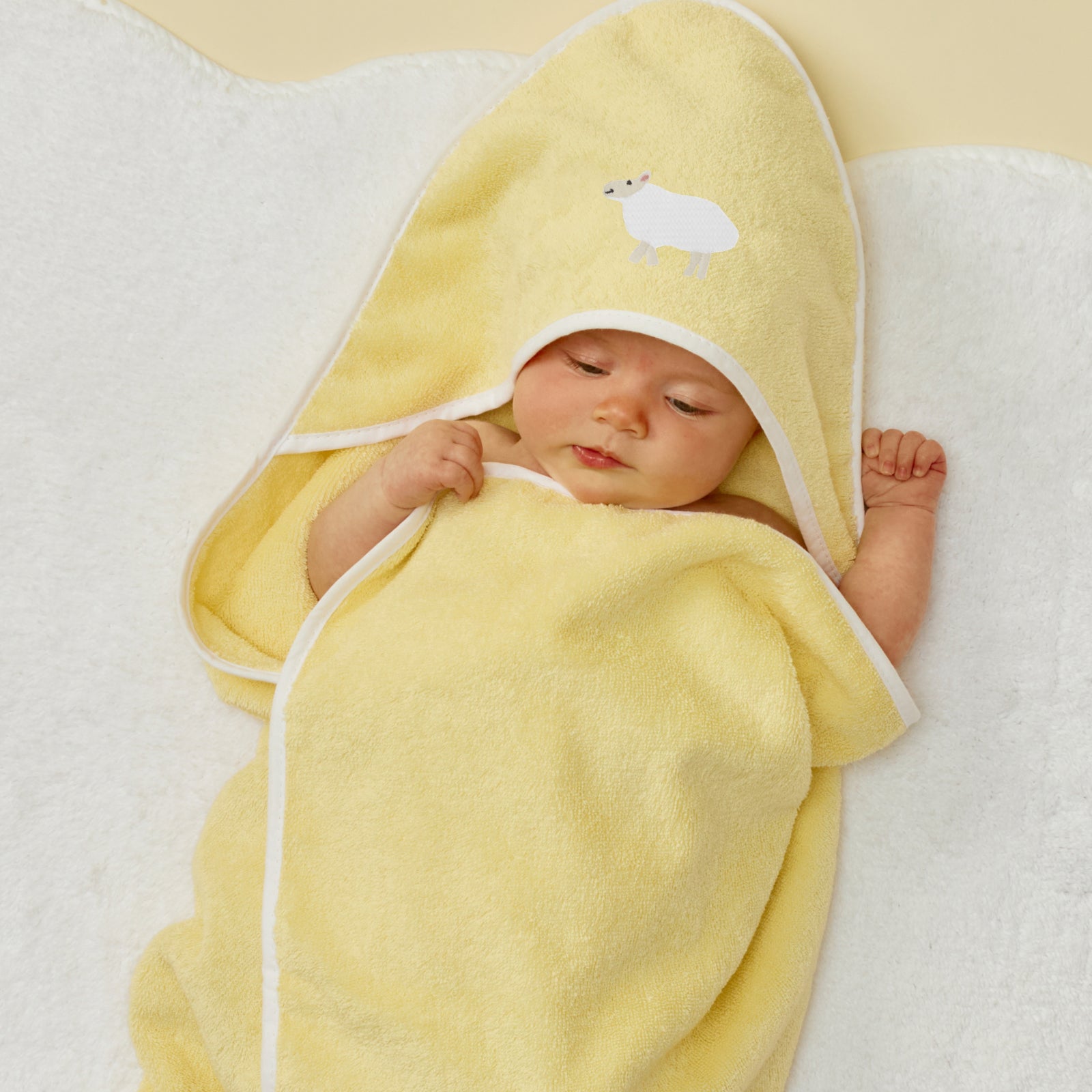 Baby wrapped in a yellow hooded towel with white trim and lamb embroidery.