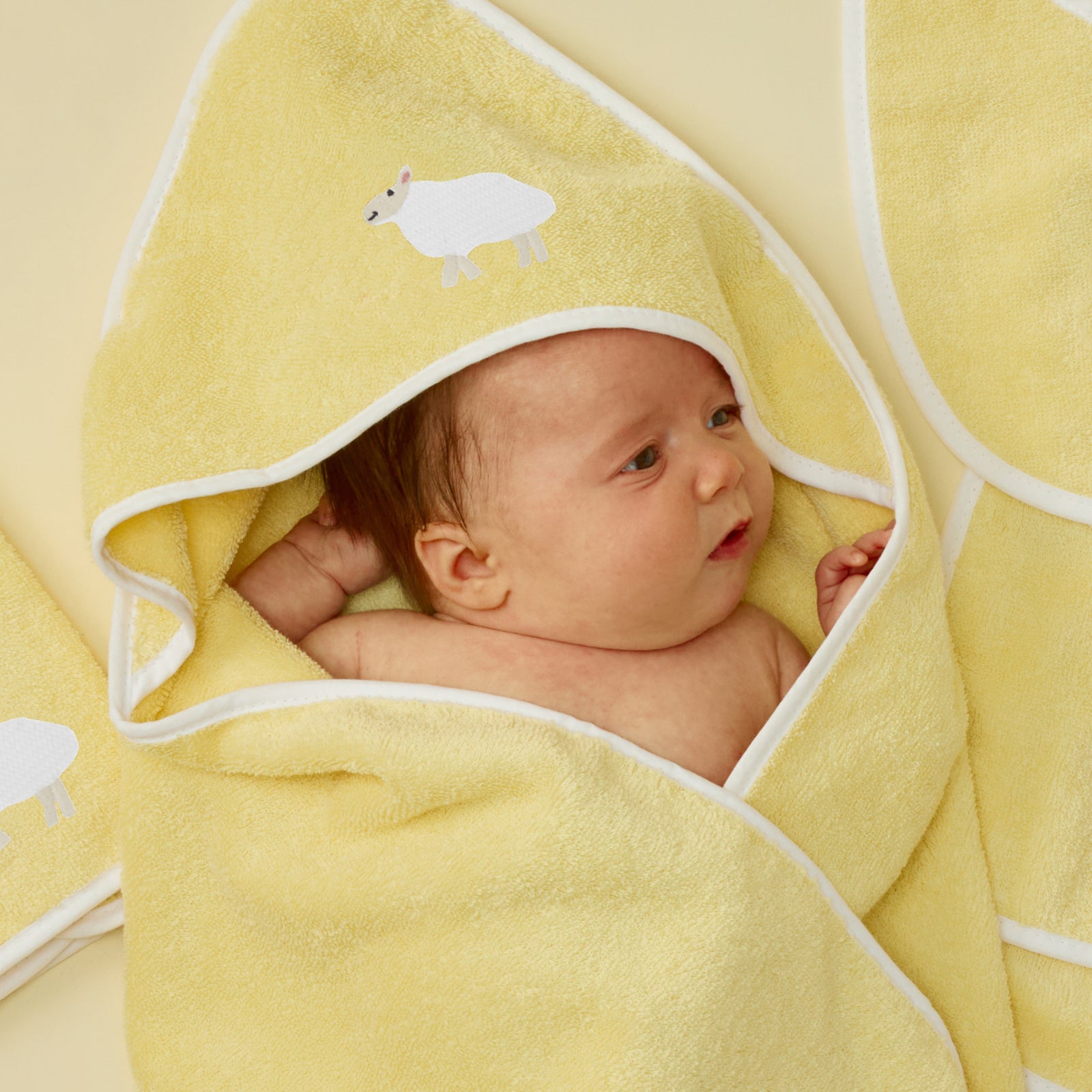 Baby wrapped in a buttercup yellow hooded towel with white piping and lamb embroidery.
