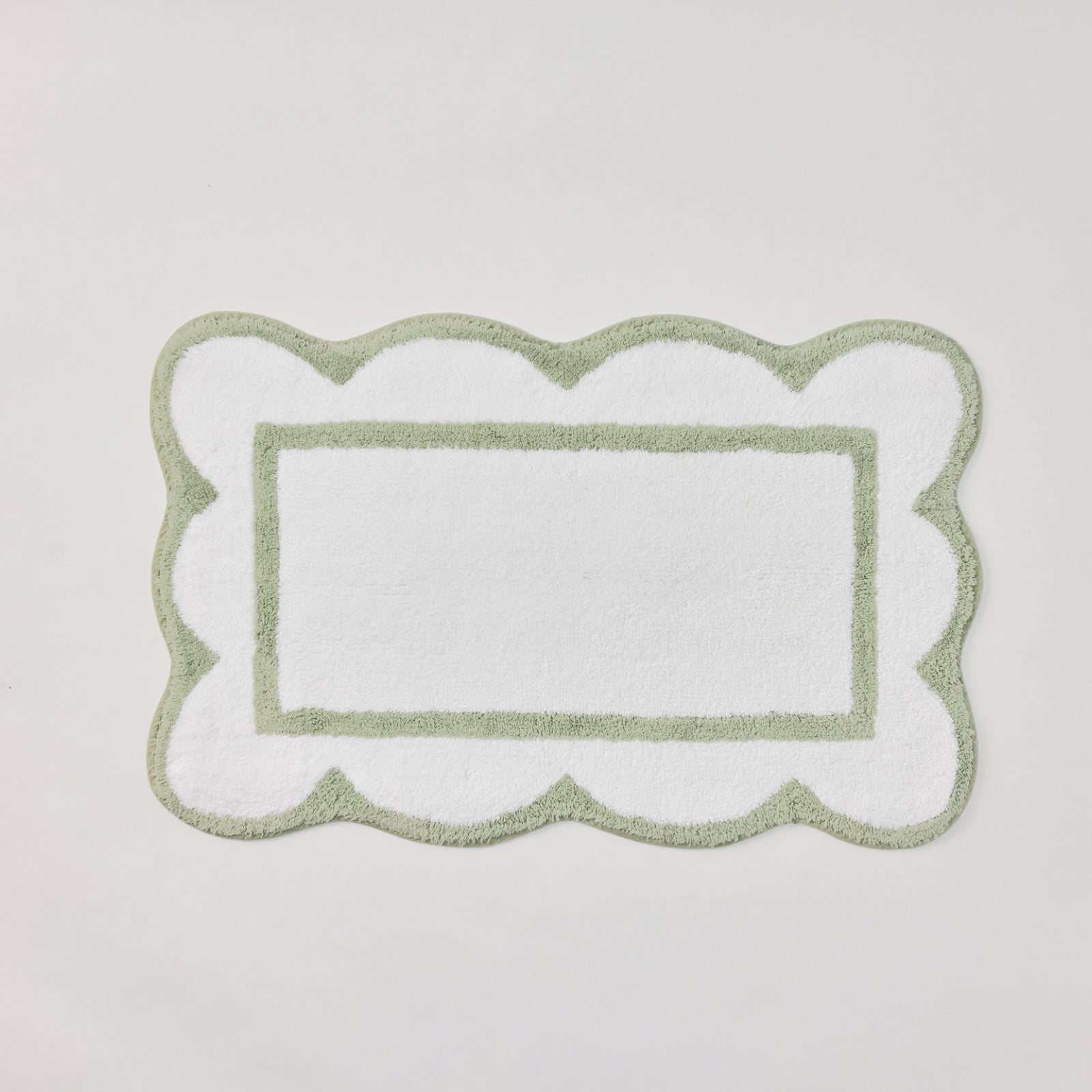 A rectangular white bath mat with a scalloped border and a central rectangular cutout, shown on a light gray background.