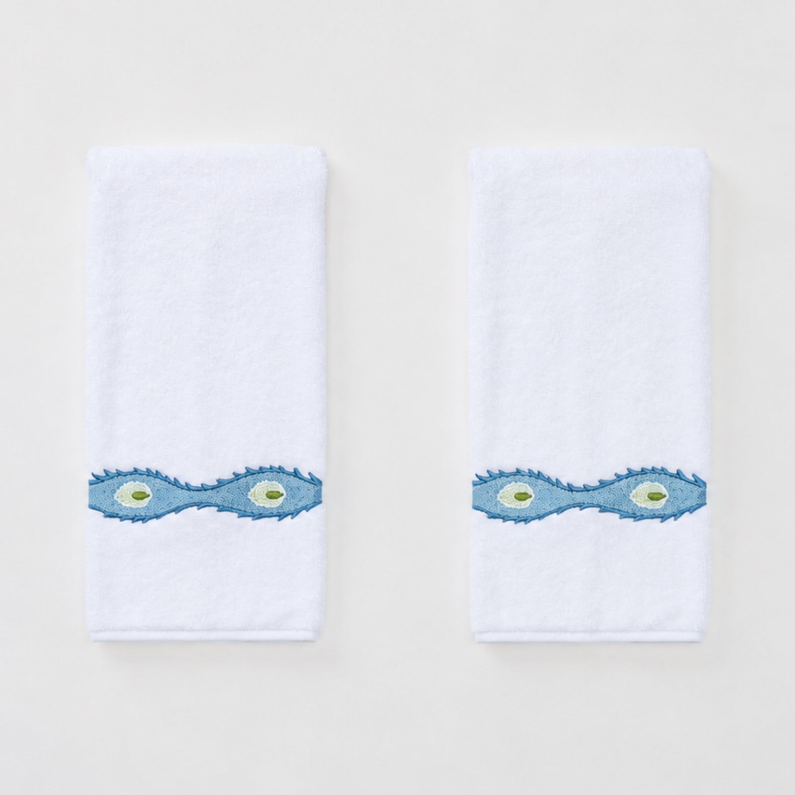 Two white Weezie hand towels with wavy blue Lee Jofa Marciana embroidery on a white background.