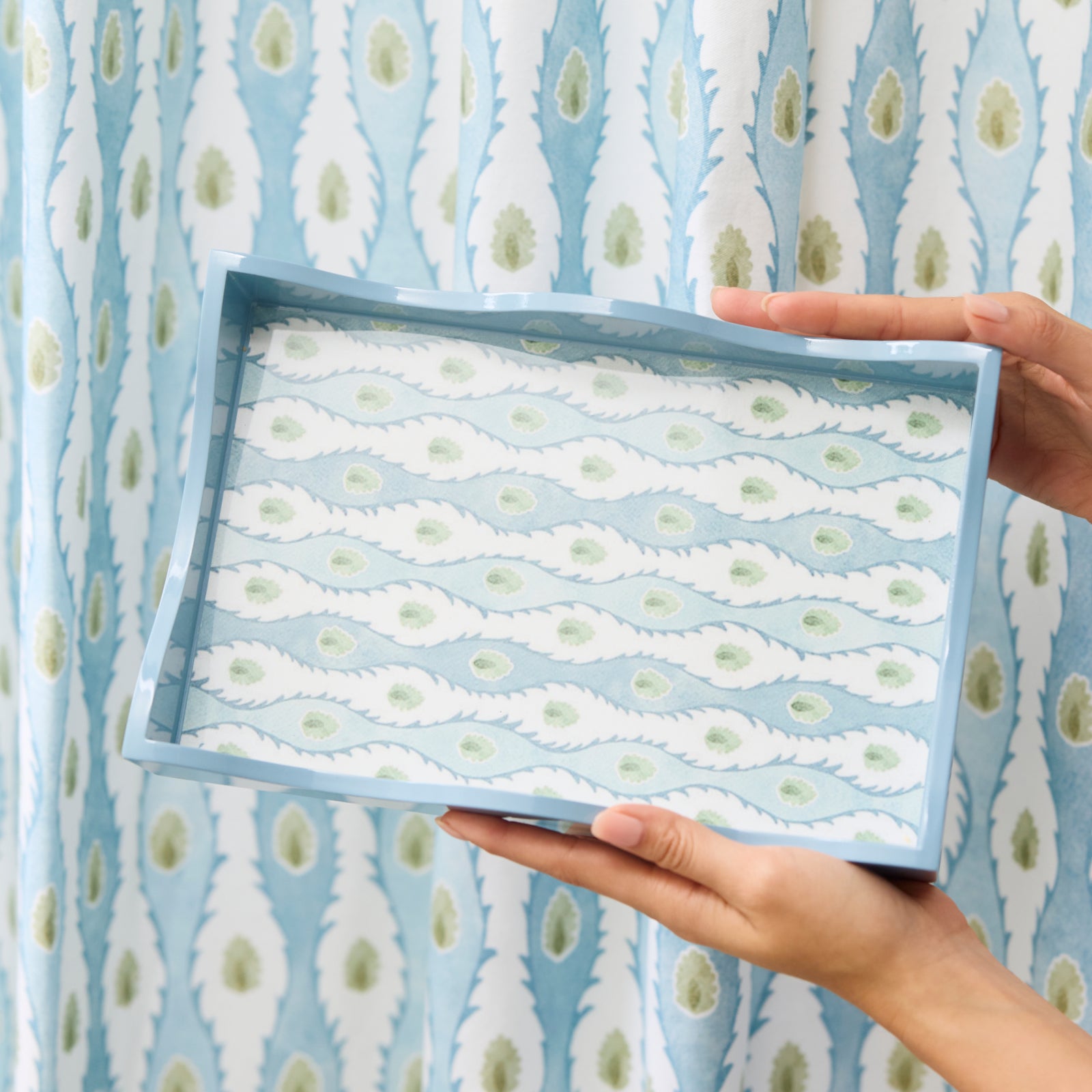 Hands holding a blue Lee Jofa x Weezie lacquer tray with the Marciana floral pattern.