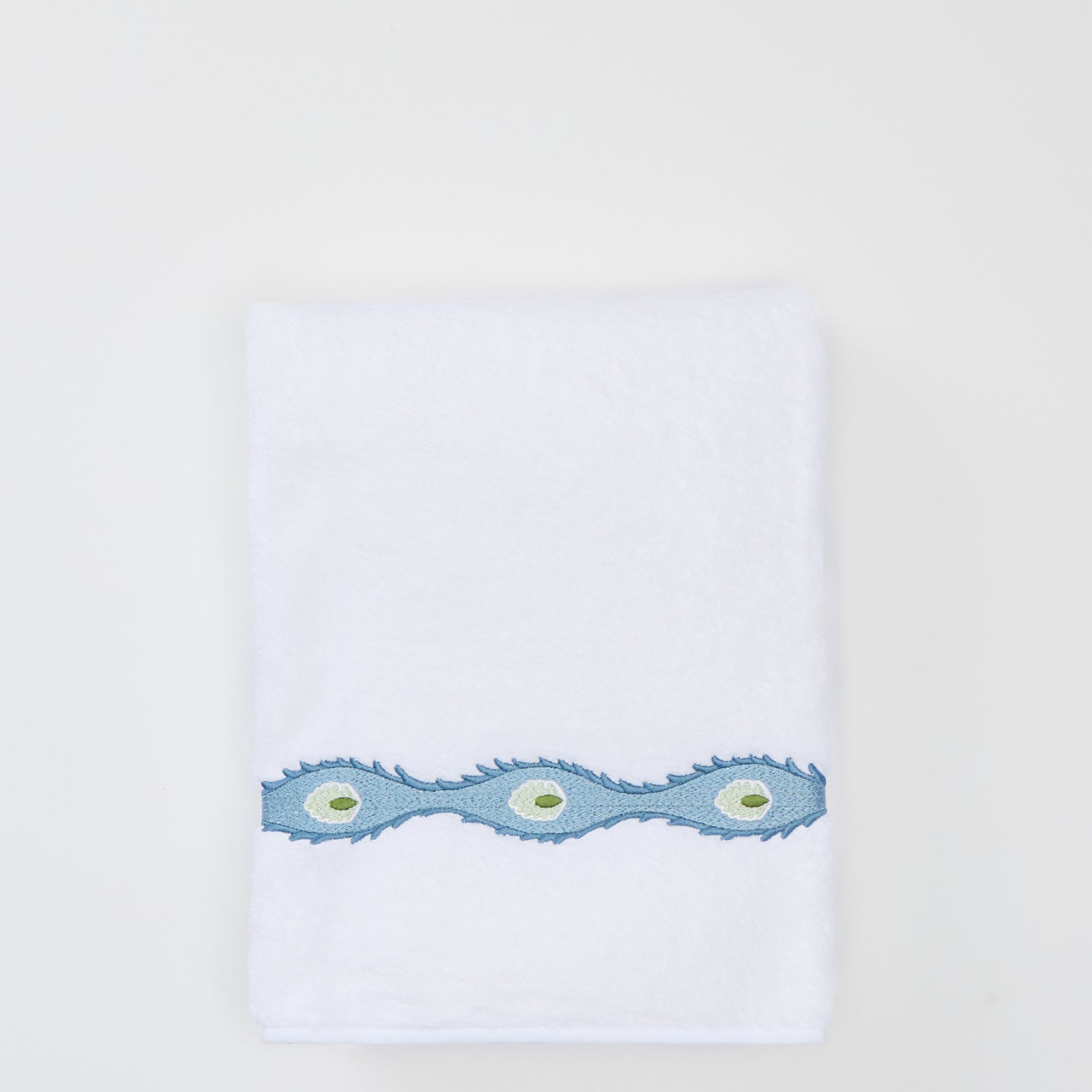 Folded white bath towel with a light blue wavy embroidered trim featuring green oval motifs.