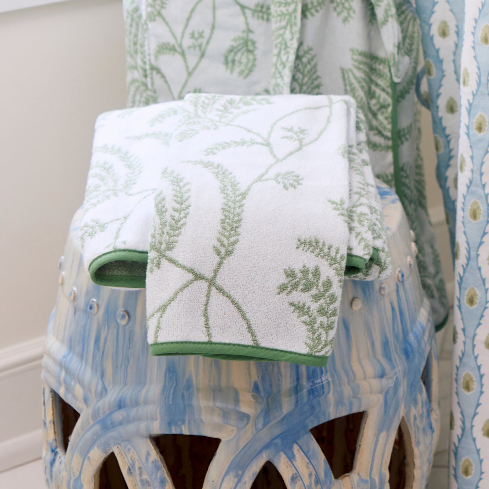 Folded white towels featuring a sage green Lee Jofa Palmero floral pattern with green piped edges.