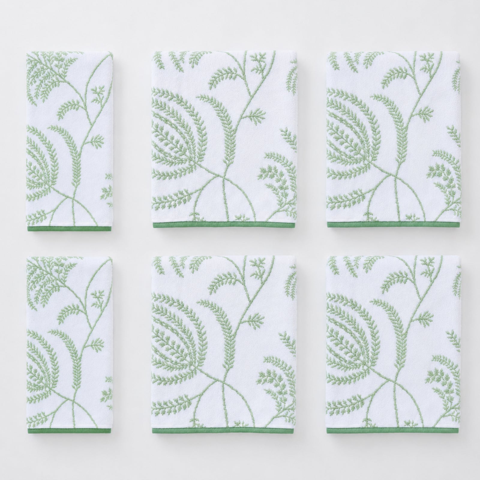 Sage green and white Palmero floral patterned towels neatly folded inside a wooden cabinet.