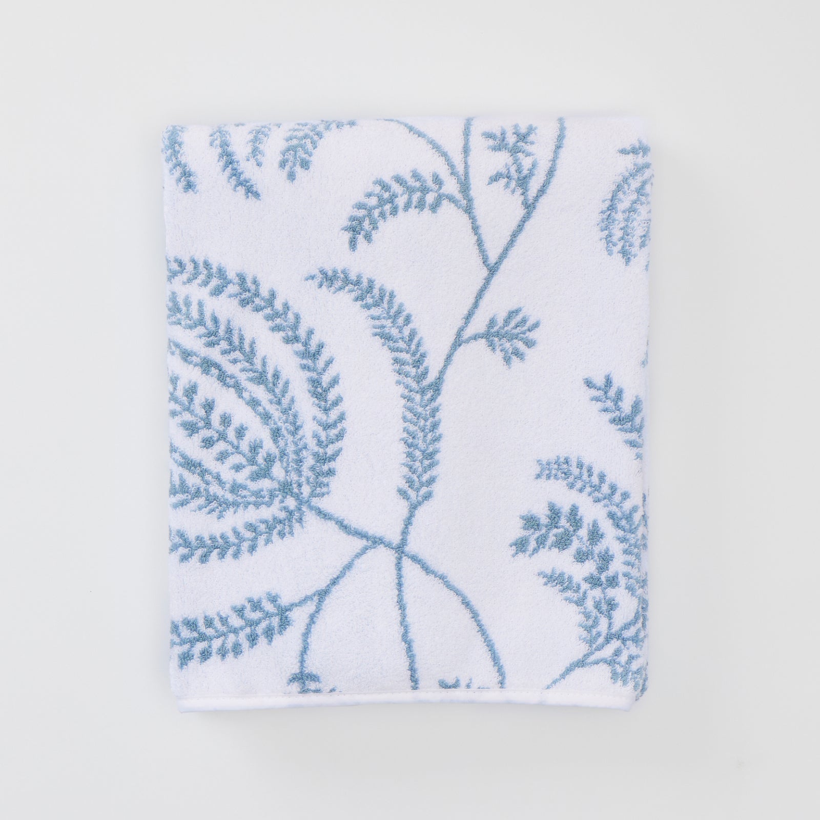 A folded white bath towel featuring a delicate light blue Palmero botanical pattern