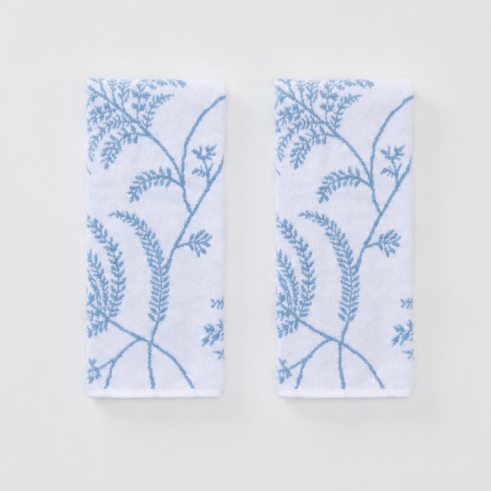 Two white hand towels with a light blue Palmero botanical pattern laid flat side by side.