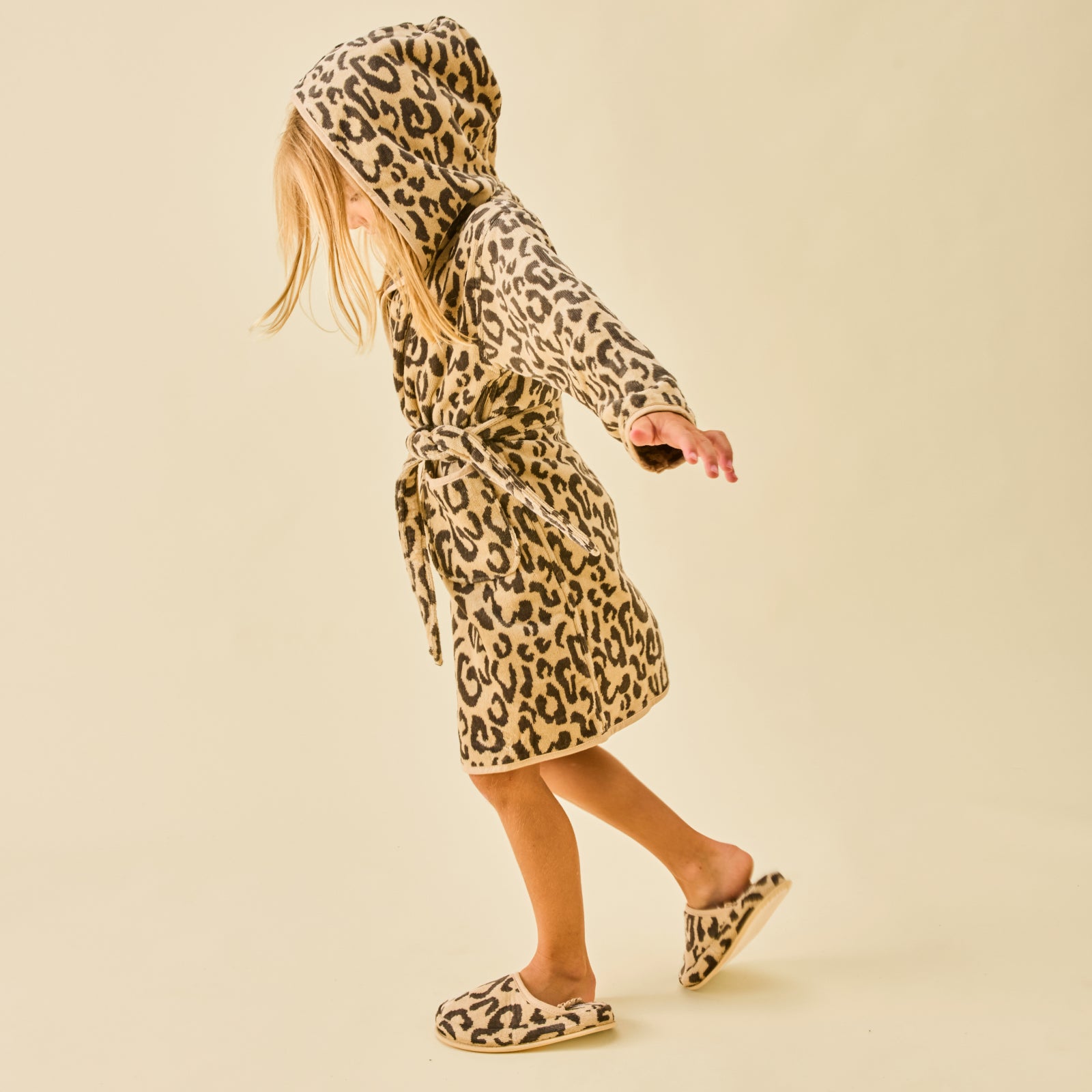 A young girl wearing a hooded leopard print plush bathrobe and matching fluffy slippers.