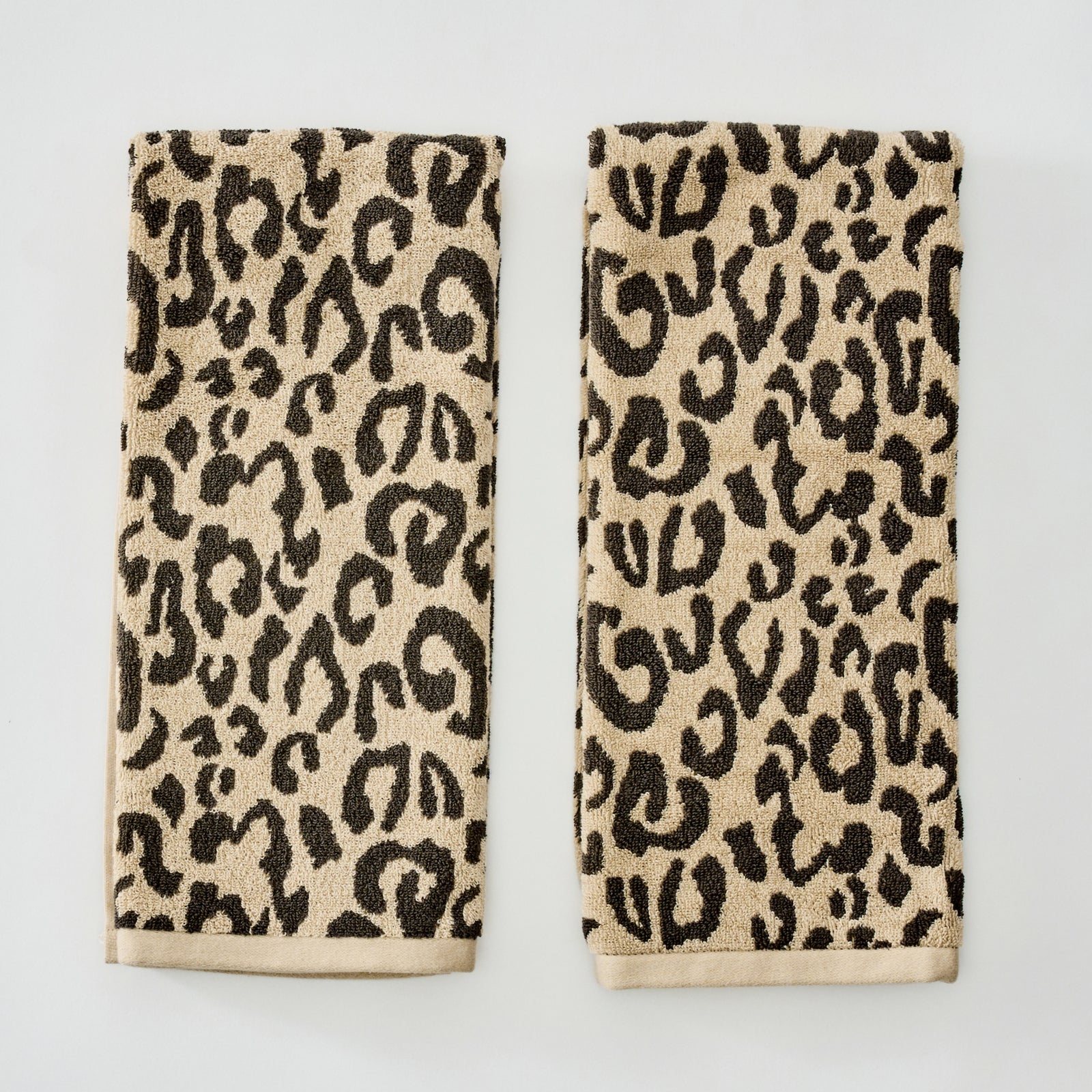 Two rectangular beige towels with a black leopard print pattern and solid beige borders, displayed side-by-side on a light gray background.