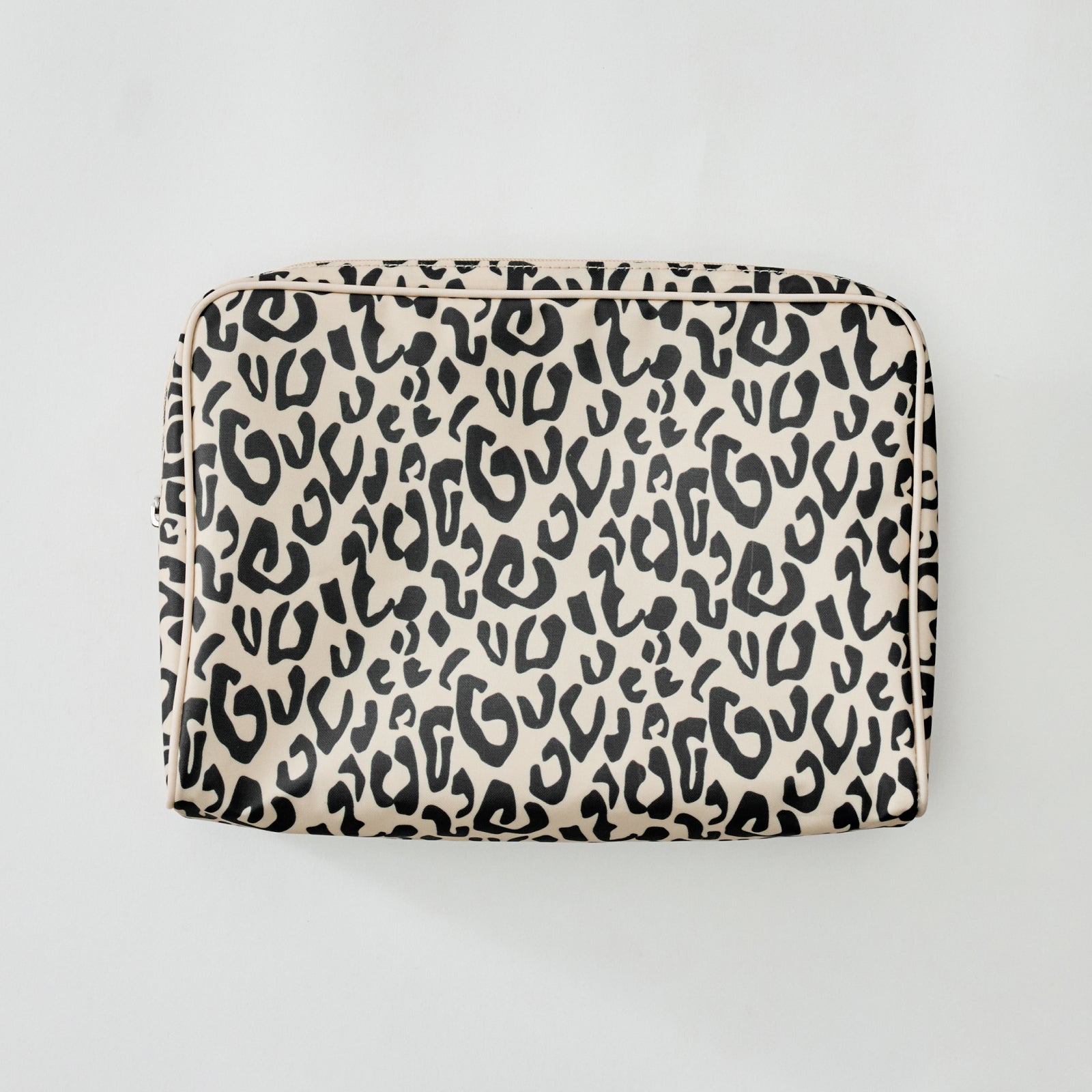 A rectangular zippered pouch with an all-over black leopard print on a warm beige background, photographed from directly above on a light gray background.