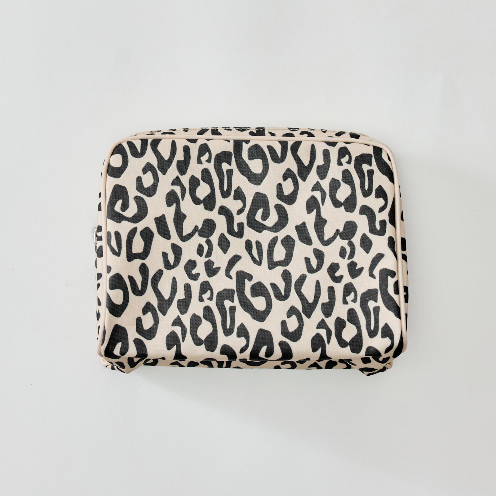 A rectangular zippered pouch with a black leopard print pattern on a warm beige background, photographed from directly above on a light gray surface.