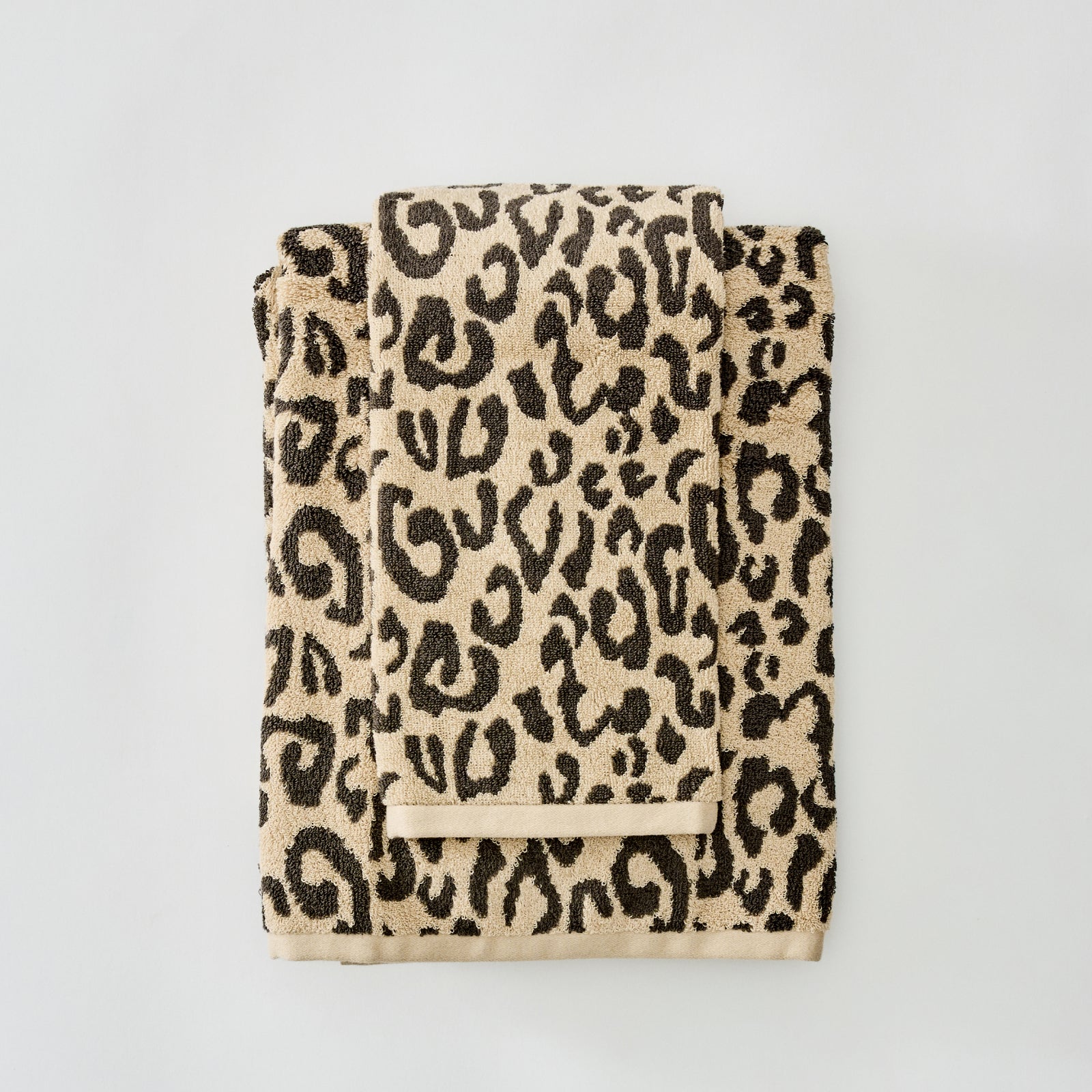 A folded beige towel with a black leopard print pattern and a matching beige loop handle, photographed on a clean light gray background.