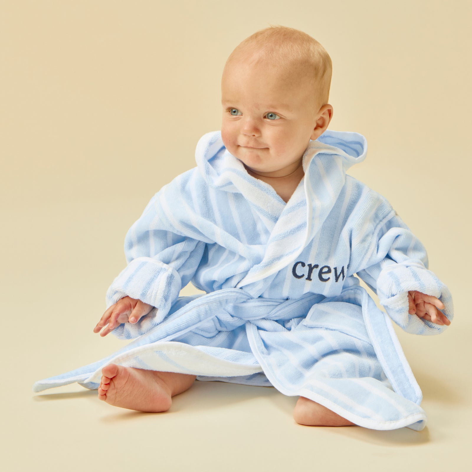 Smiling baby wearing a fluffy light blue striped bathrobe with "crew" embroidered on the front.