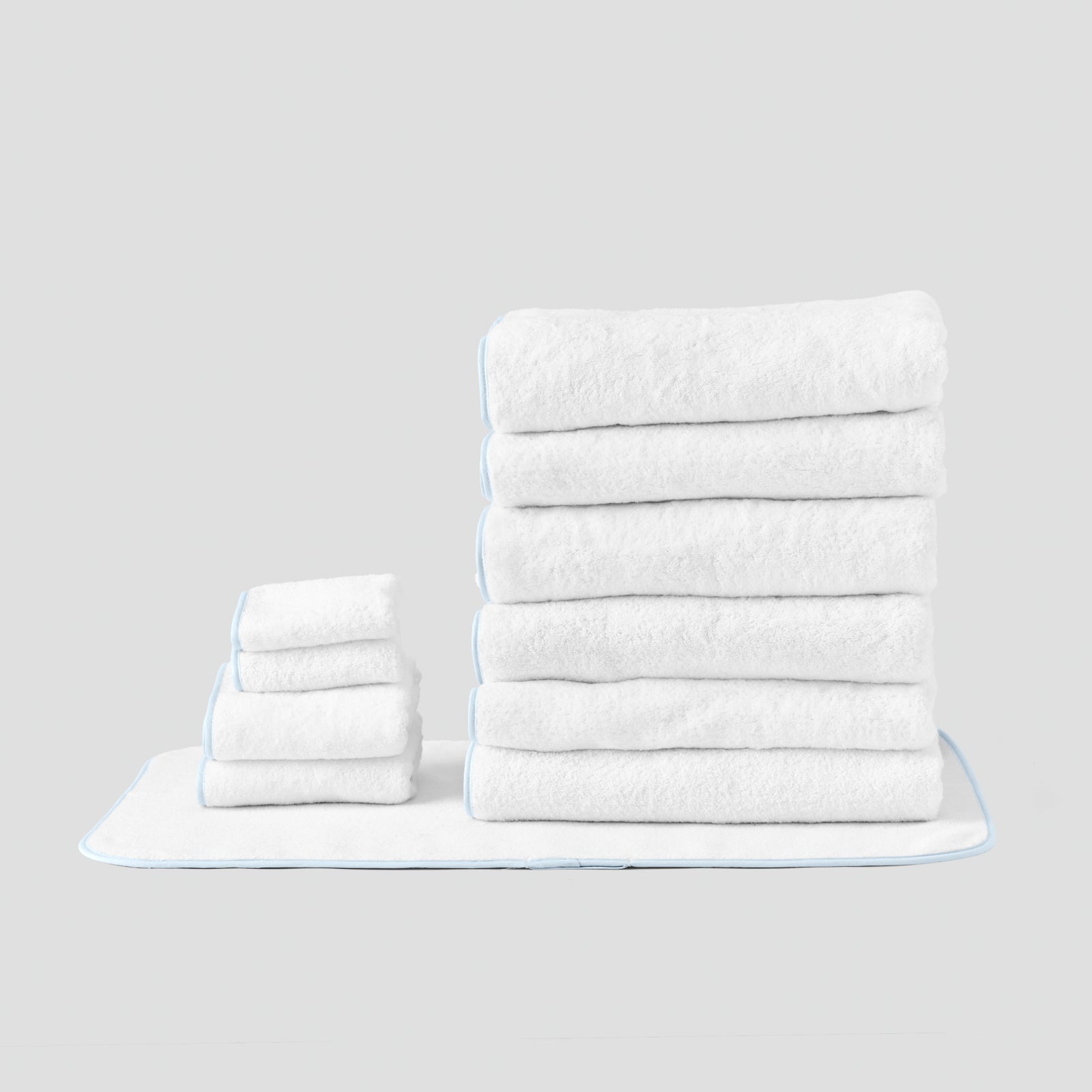 Signature Bathroom Bundle in Light Blue on White, folded white towels and bath mat with light blue piping.
