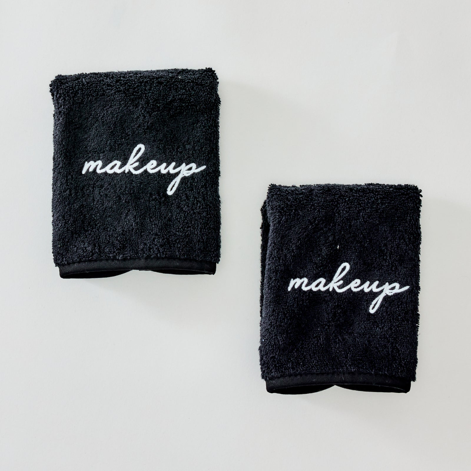 Two black microfiber makeup remover cloths with the word 'makeup' embroidered in white script, displayed on a clean white background.