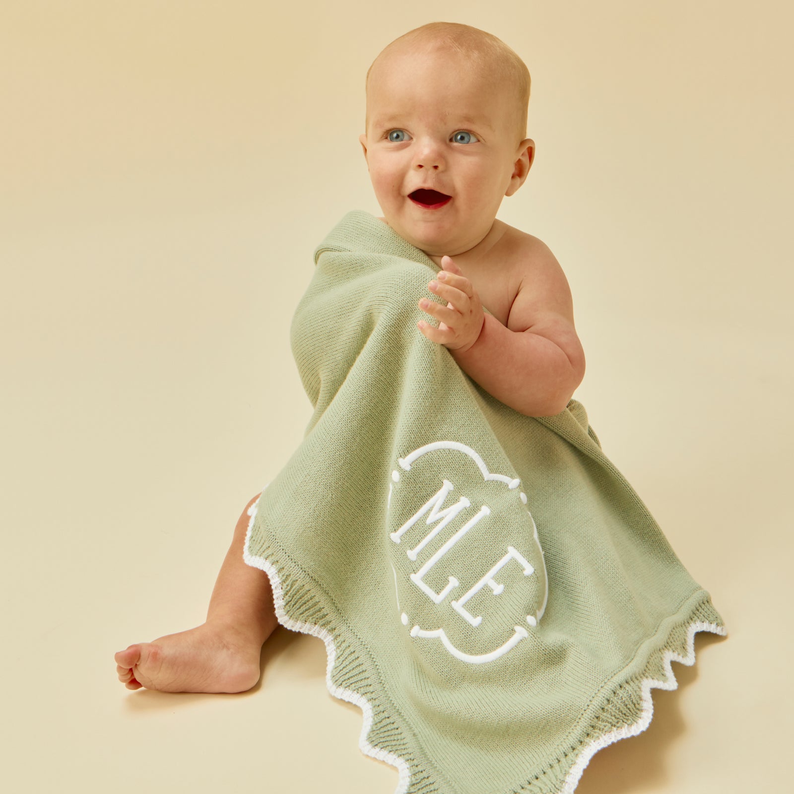 Smiling baby wrapped in a matcha green blanket with white scalloped edges and an MLE monogram.