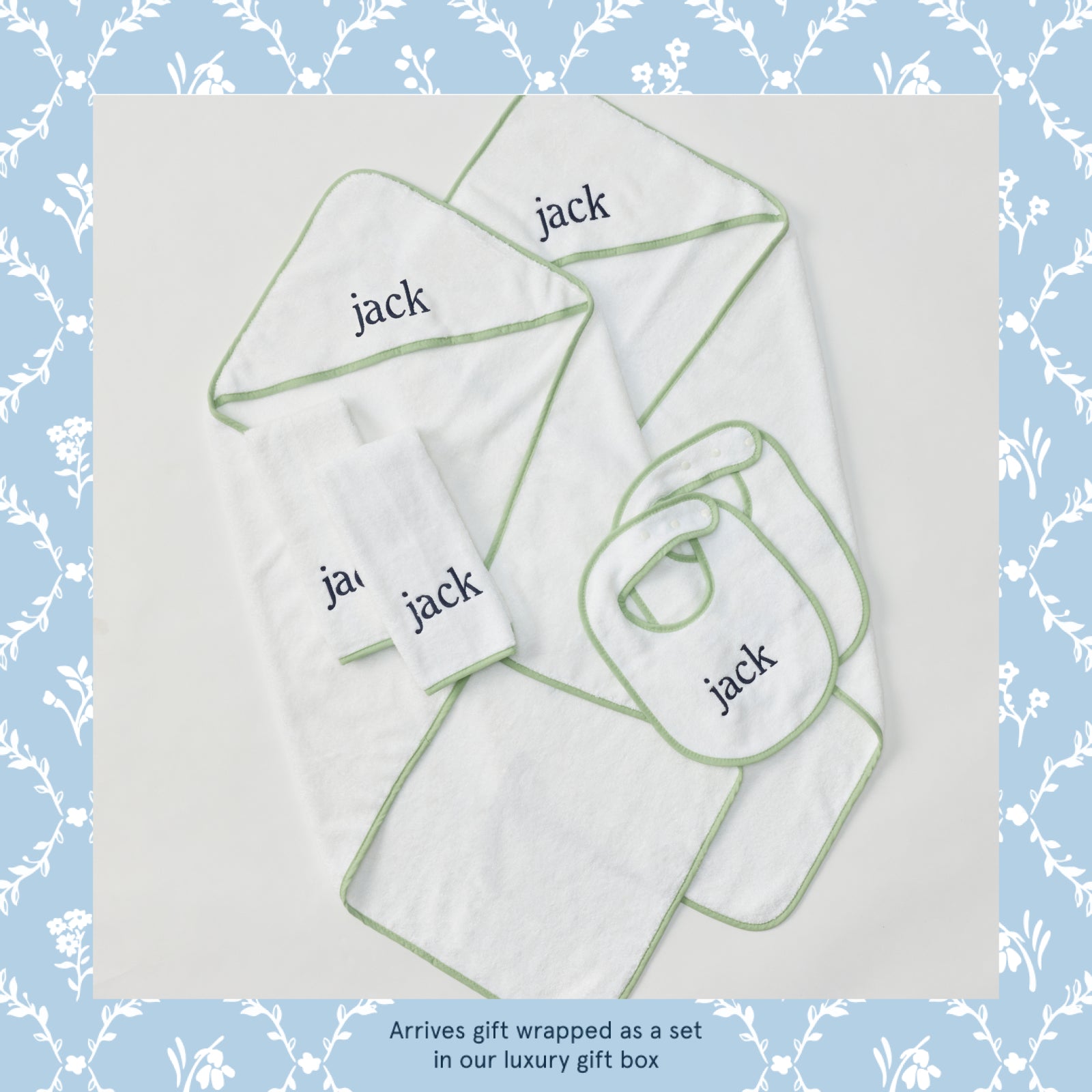 White baby towels, bibs, and burp cloths featuring green trim and blue jack embroidery.