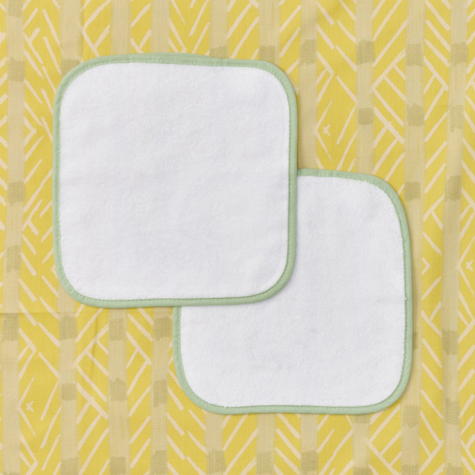 Two white baby washcloths with green piping
