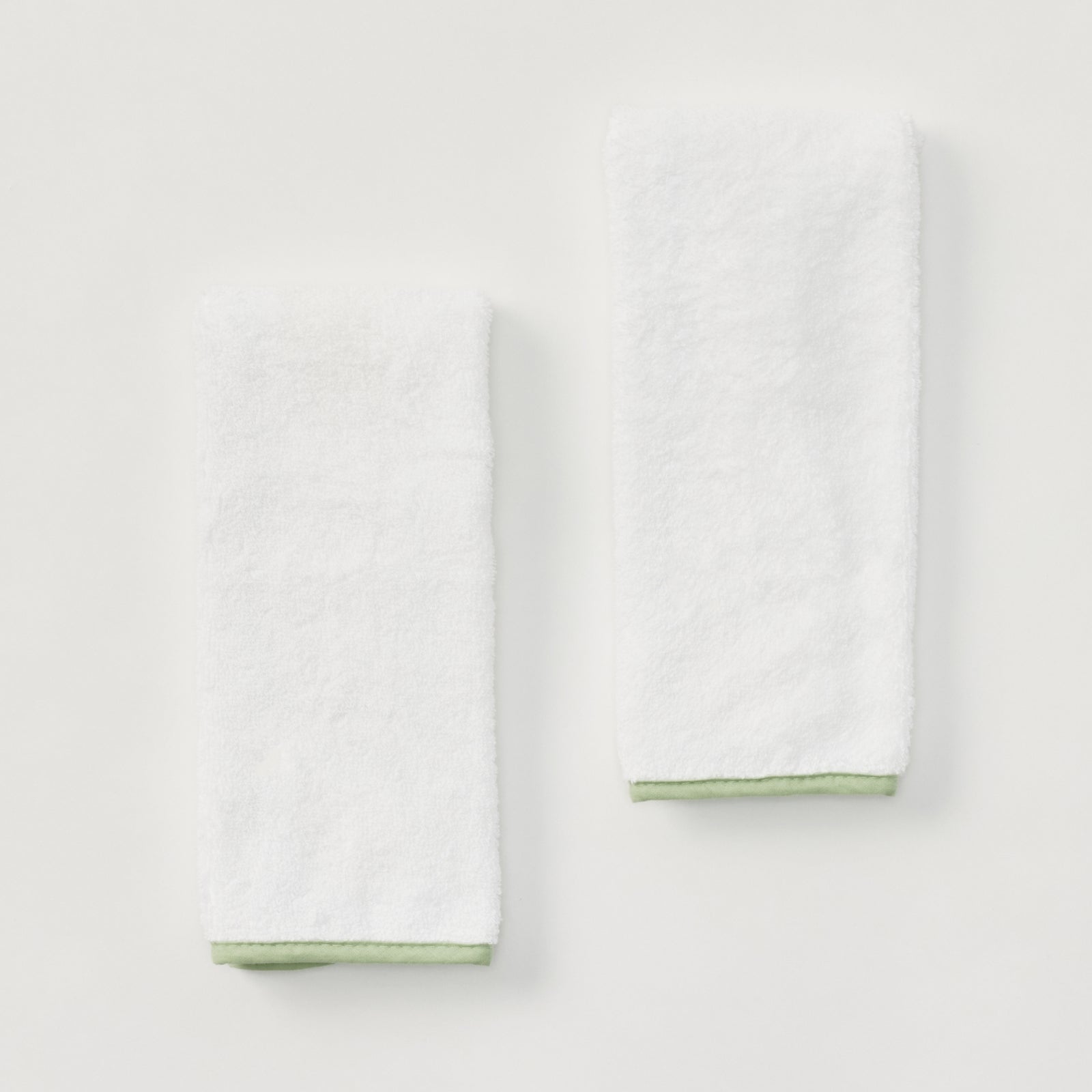 Two white baby burp cloths with matcha green edge piping.