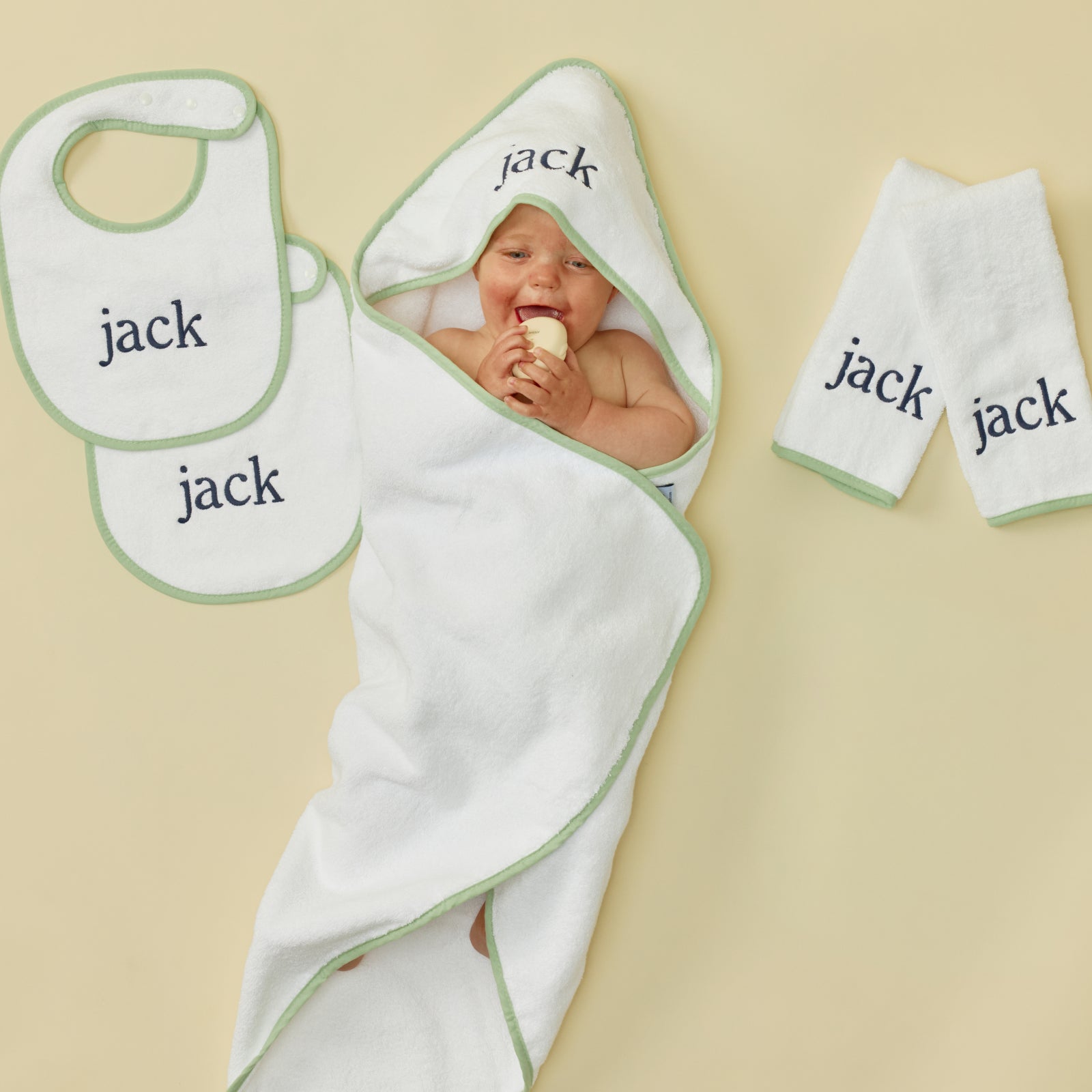 White baby towels, bibs, and burp cloths featuring green trim and blue jack embroidery.