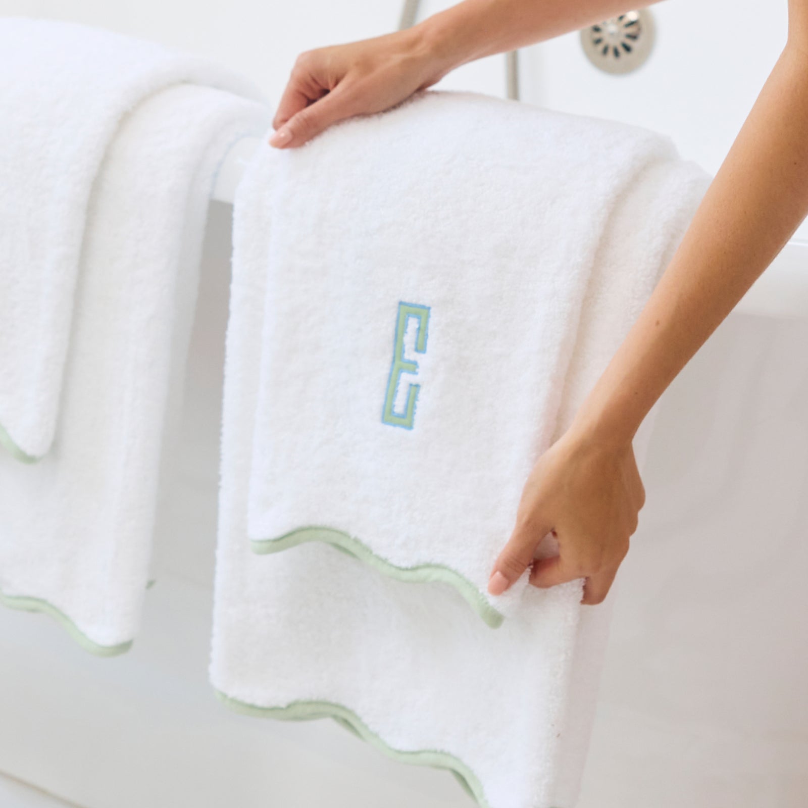 Hands holding a white hand towel with matcha green scalloped trim and an embroidered E.