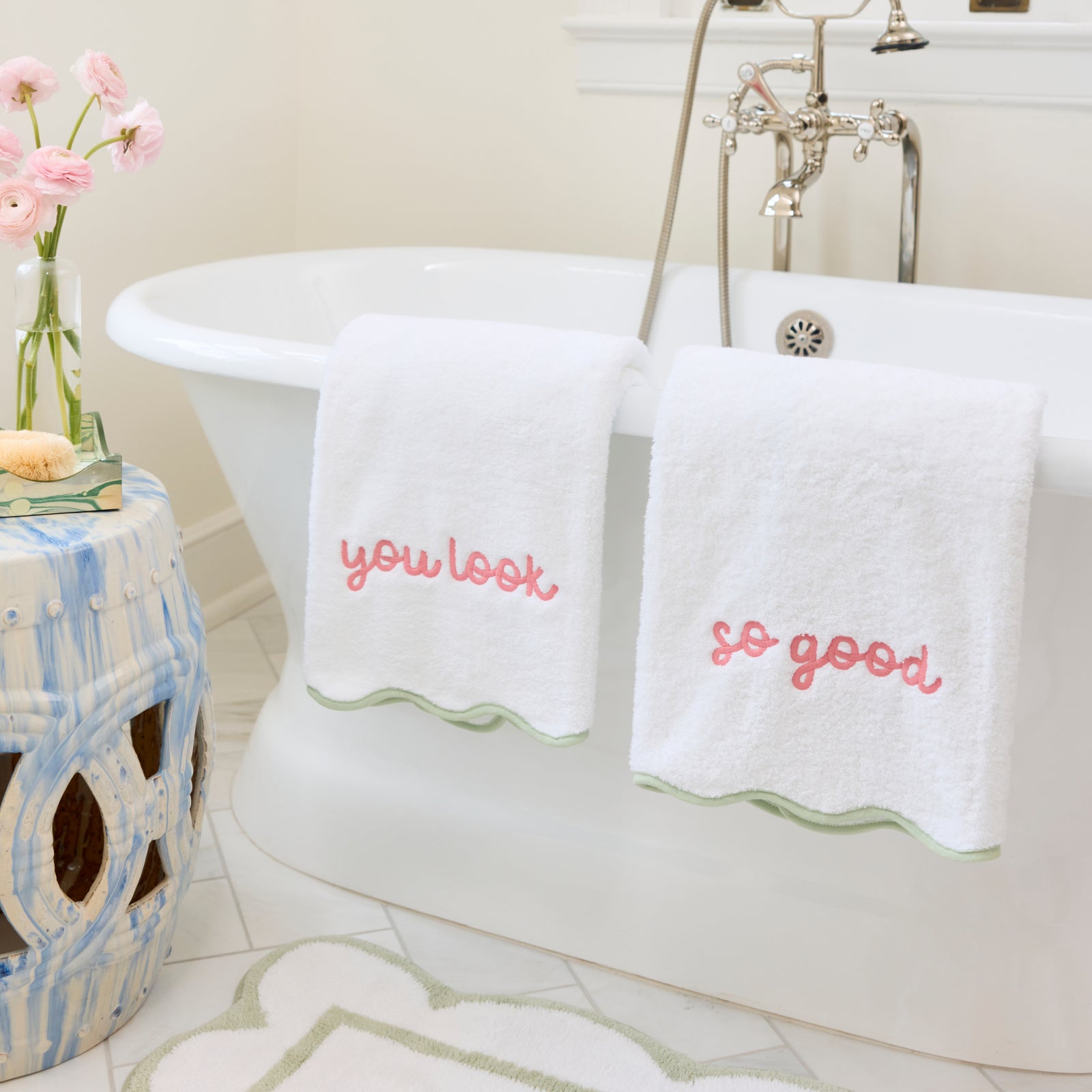 Two white towels with matcha scalloped edges and pink 'you look so good' embroidery on a tub.