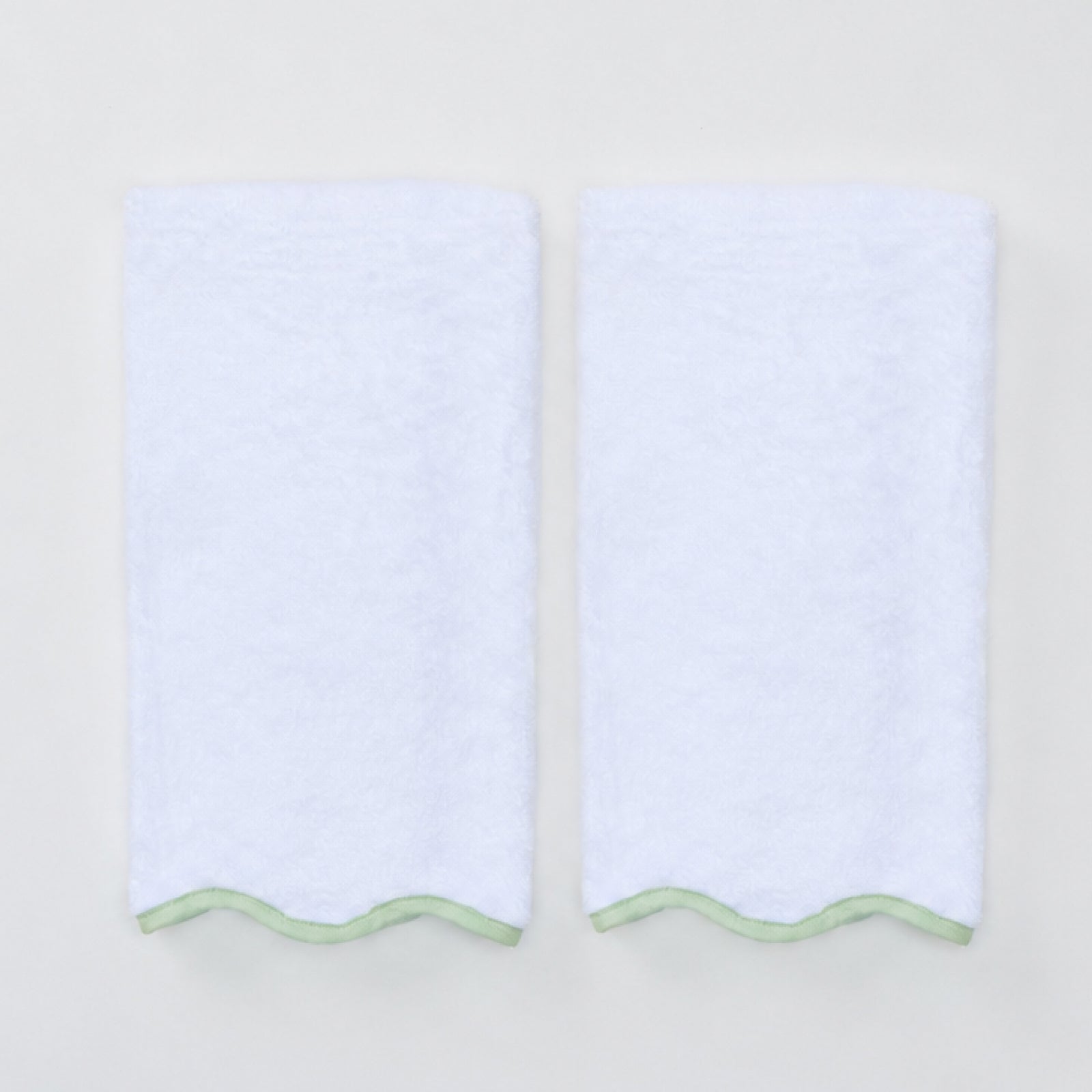 Two folded white hand towels with a matcha green scalloped trim at the bottom edge.