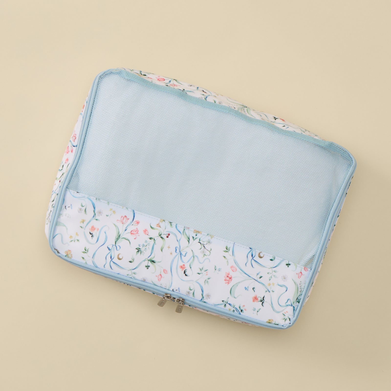 A rectangular mesh zippered travel organizer pouch with a white floral print border and a light blue interior, shown on a solid beige background.